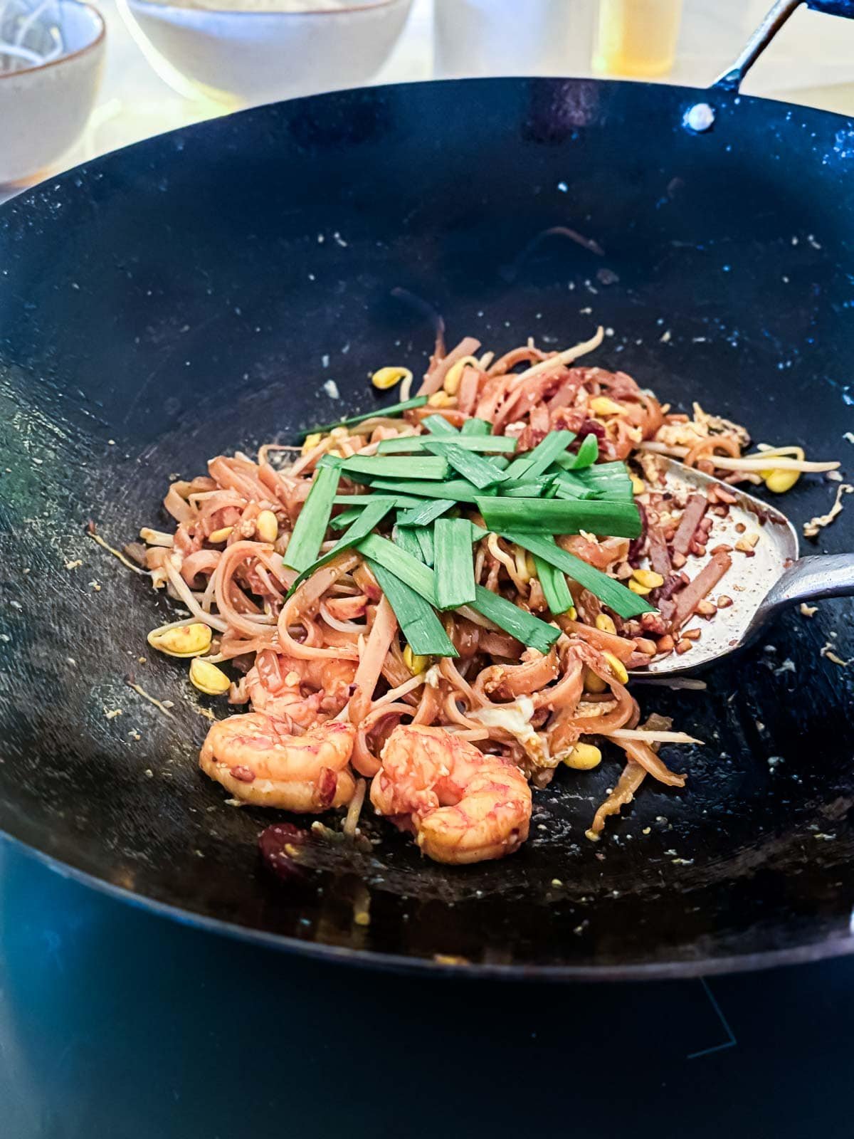 metal spatula stirring char kway teow in wok with Chinese chives added on top.