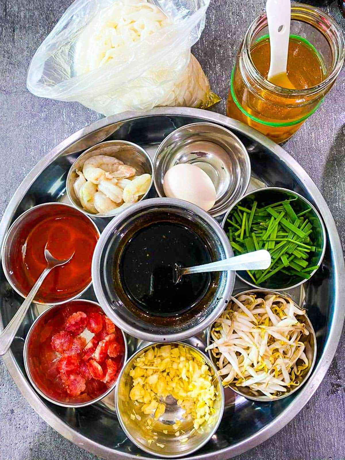 char kway teow stir fry ingredients arranged in bowls and jars - fresh noodles, lard, egg, chives, sprouts, sausage, prawns, chili garlic sauce, stir fry sauce.