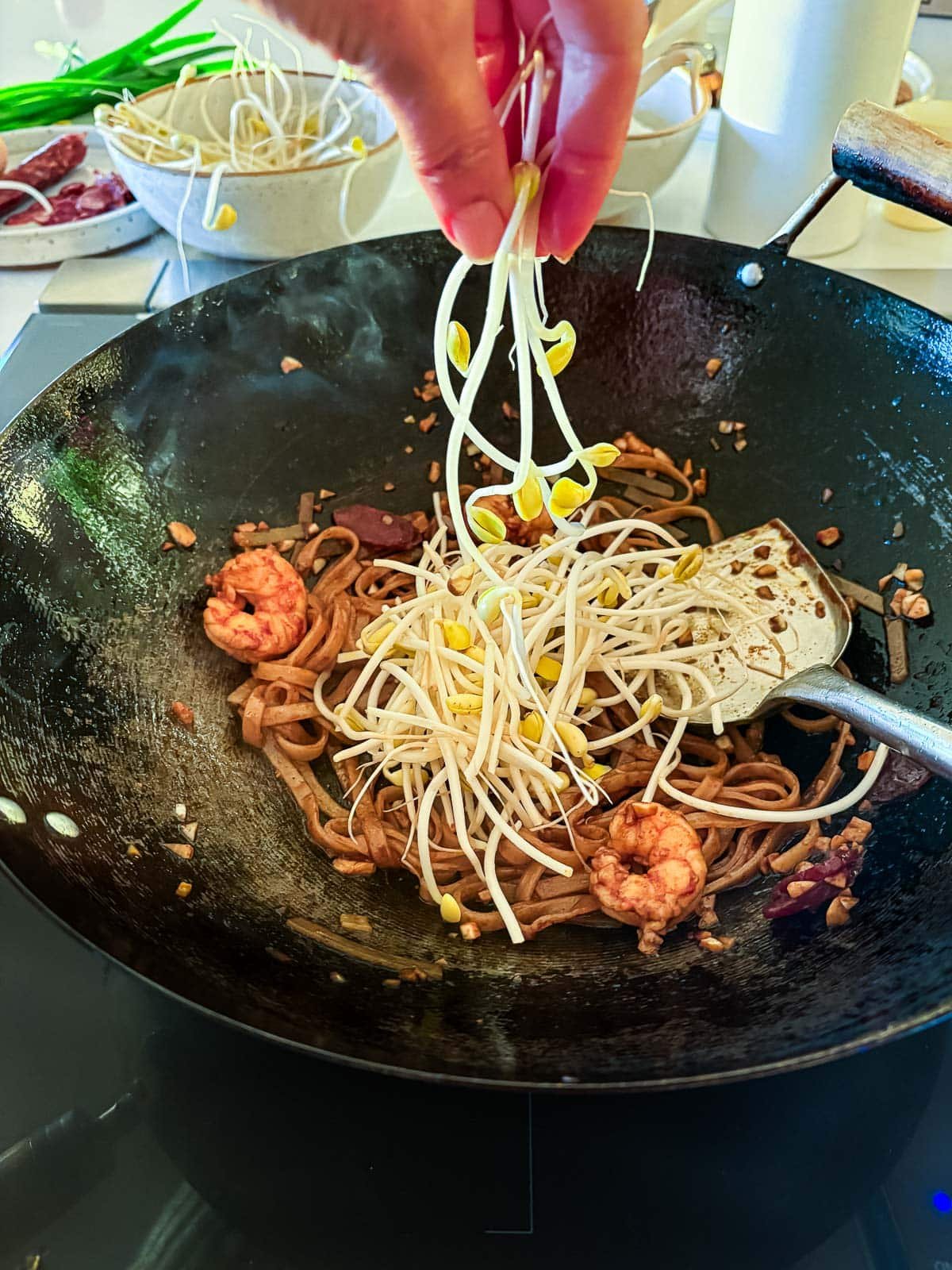 adding fresh bean sprouts to wok of char kway teow.