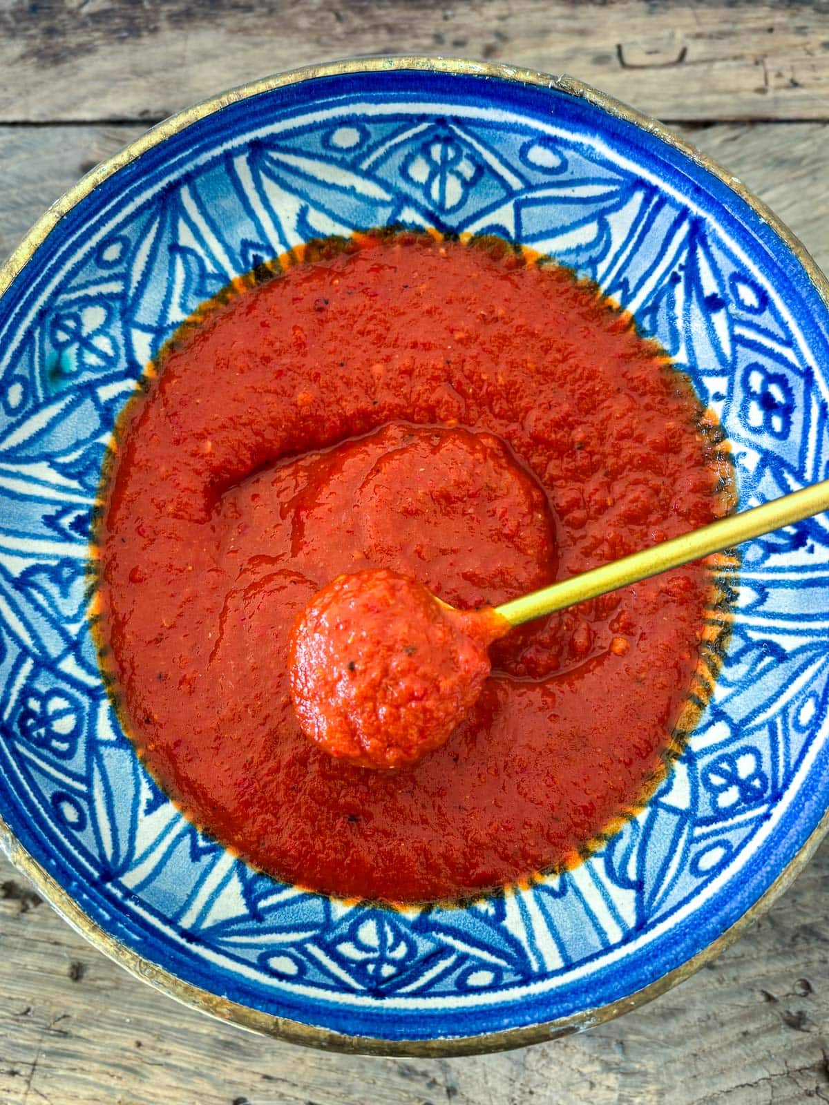 red chili garlic sauce in blue bowl with gold spoon lifting up the sauce.