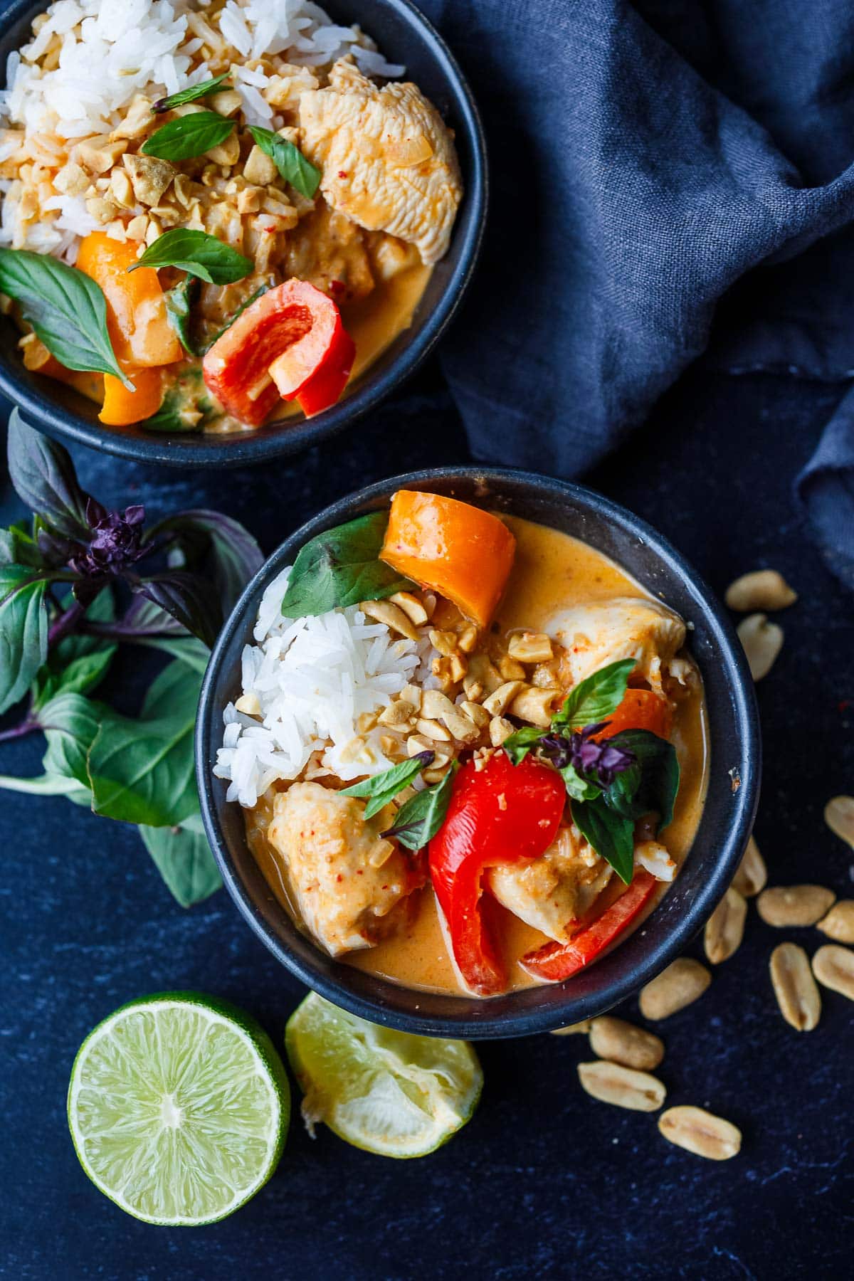 two bowls of panang curry with chicken and bell peppers serving with spoonful of jasmine rice and topped with peanuts and thai basil. 