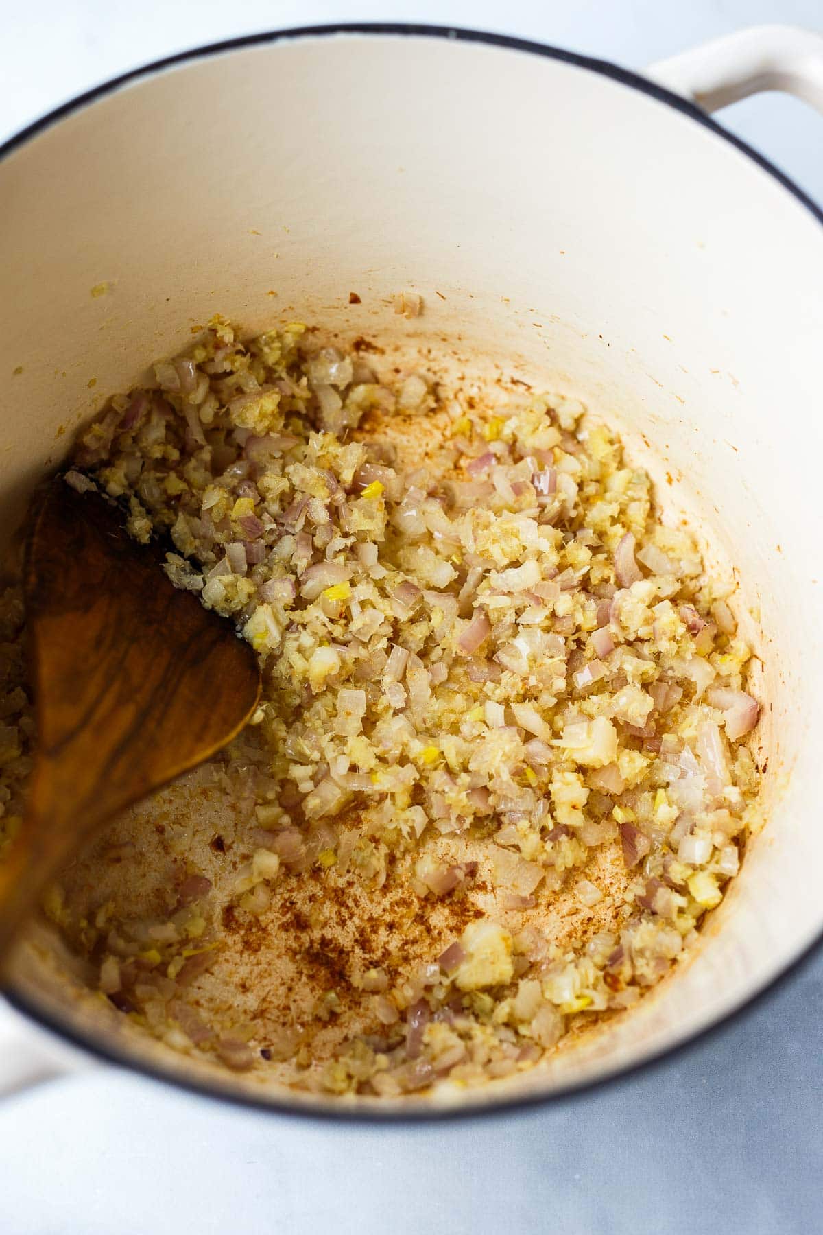 dutch oven with wood spatula stirring aromatics - garlic, lemongrass, shallot, and ginger. 