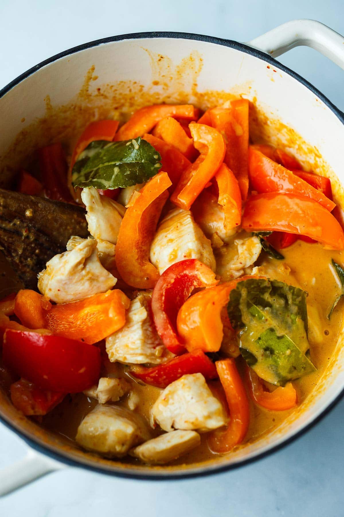 cooked down bell peppers and chicken cubes in panang curry with thai basil leaves in dutch oven. 