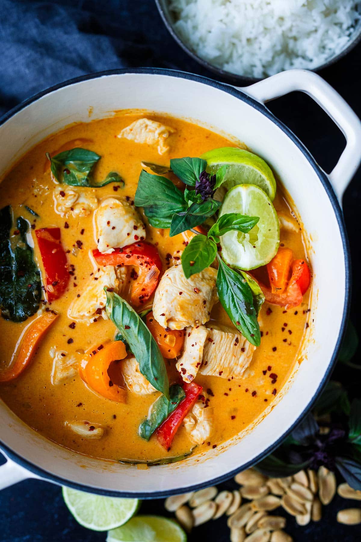 dutch oven with panang curry with chicken, bell peppers, thai basil leaves, and limes.