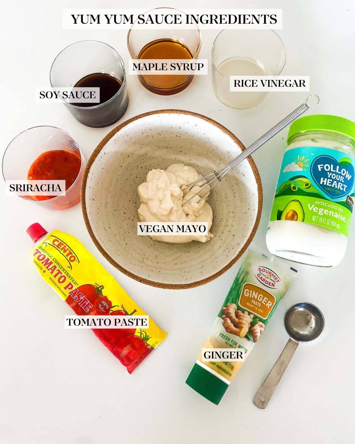 ingredients for yum yum sauce - ginger paste, tomato paste, jars of chili garlic sauce, soy sauce, maple syrup, and rice vinegar, and vegan mayo surrounding ceramic bowl with mayo and whisk.