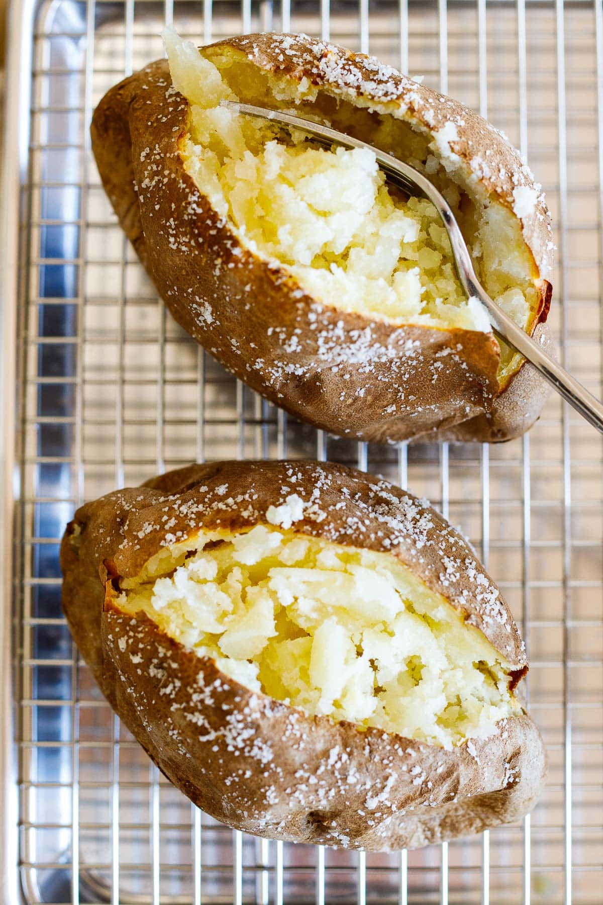 baked potato cut open to reveal fluffy interior with a fork laying down the center next to another baked potato. 