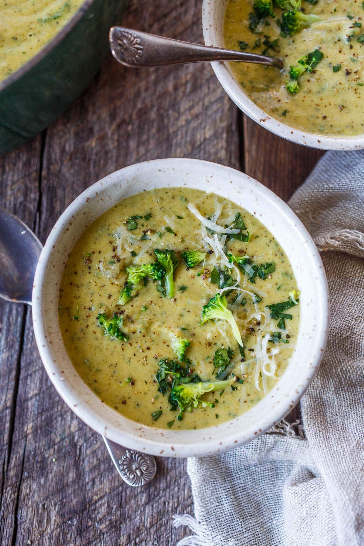 soup bowls with broccoli cheddar soup garnished with fresh broccoli pieces, fresh herbs, and grated cheese.