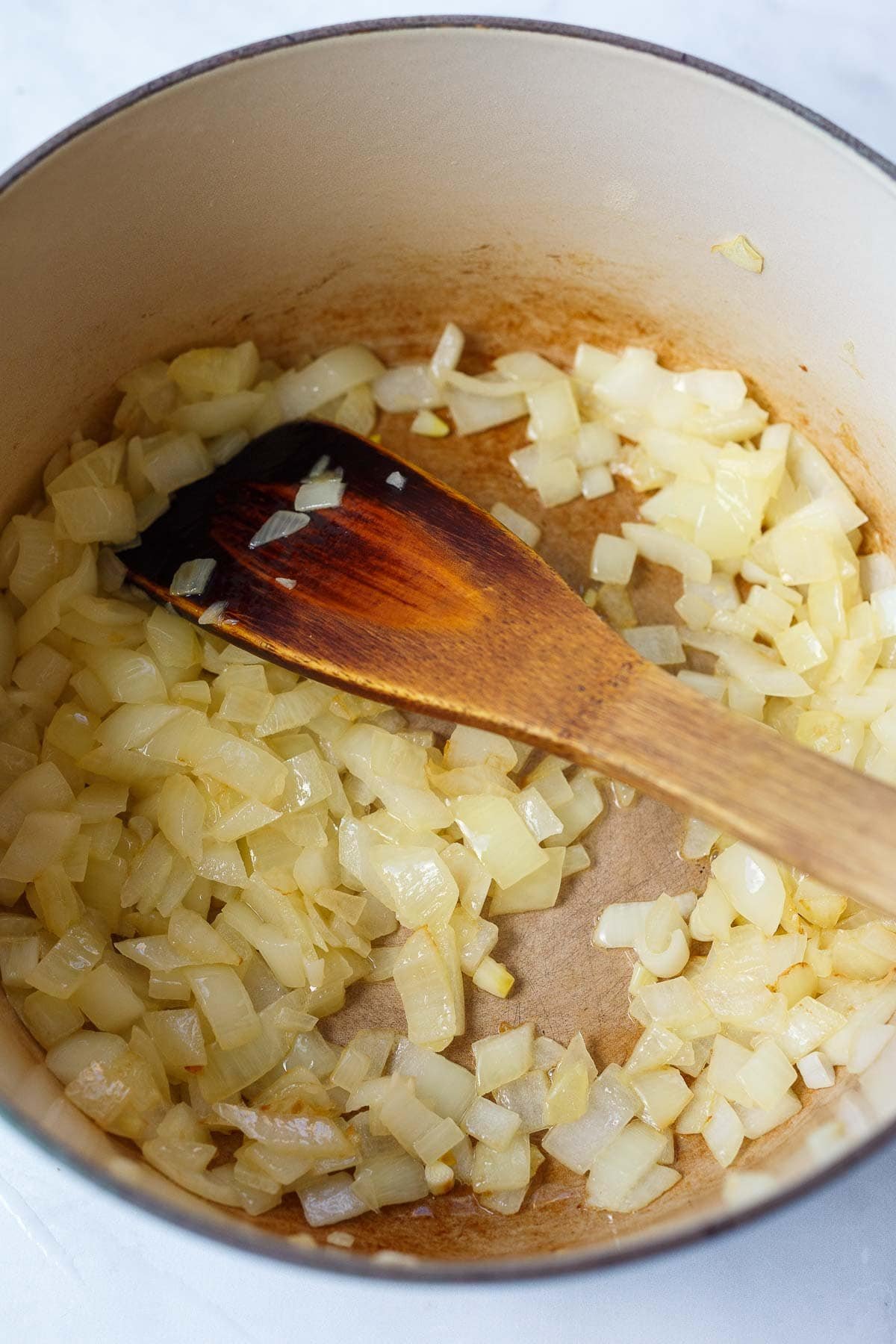 dutch oven with diced onions sautéing with wooden spatula to stir.