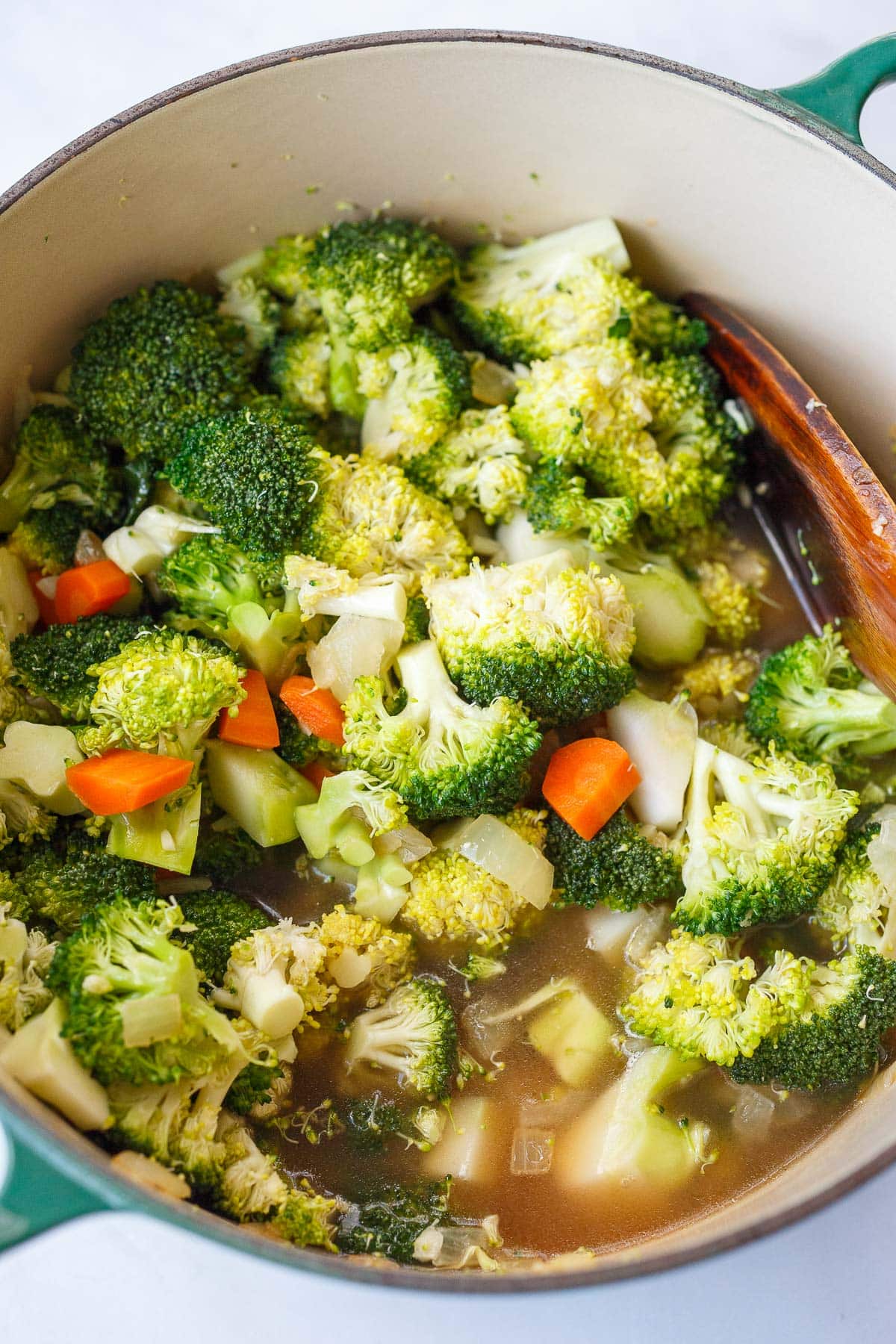 dutch oven with broccoli florets added to pot with broth, carrots, and onions.