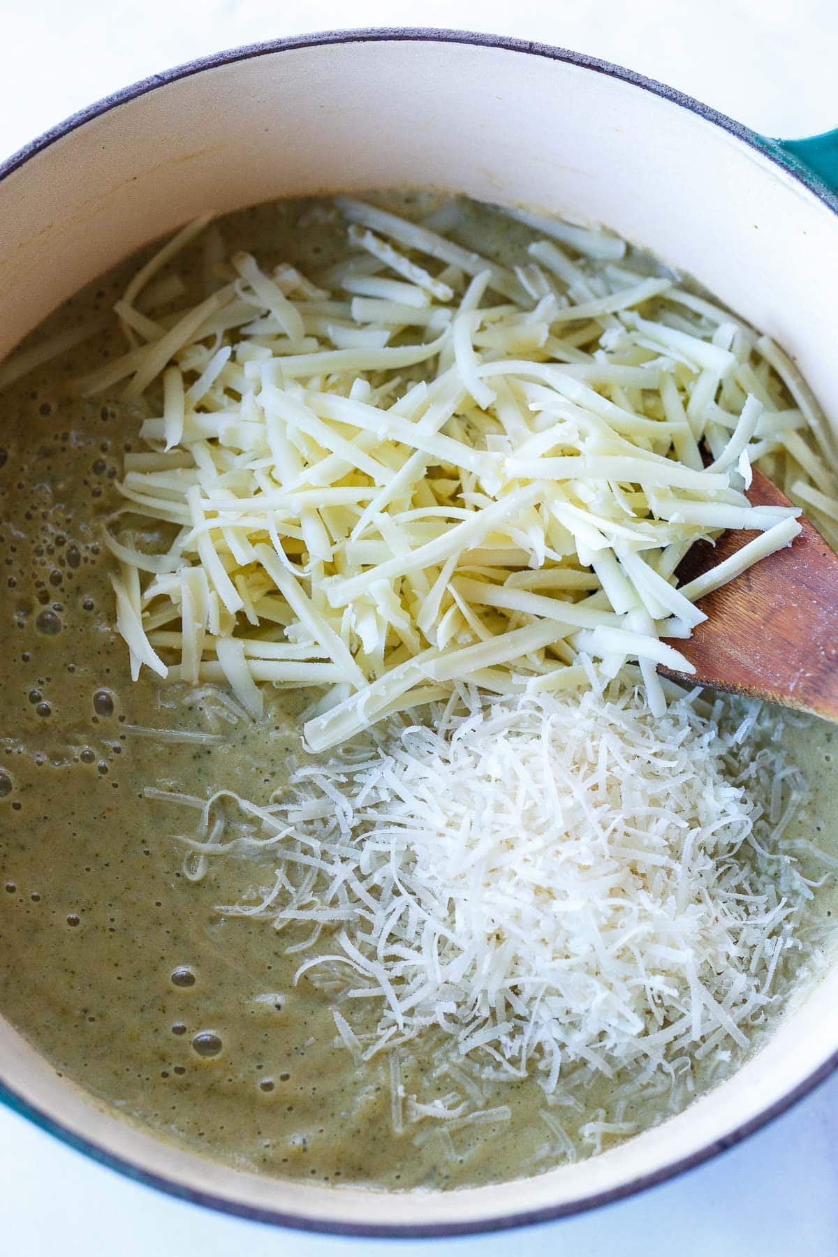 soup pot with grated cheddar and parmesan melting on top of broccoli cheddar soup.