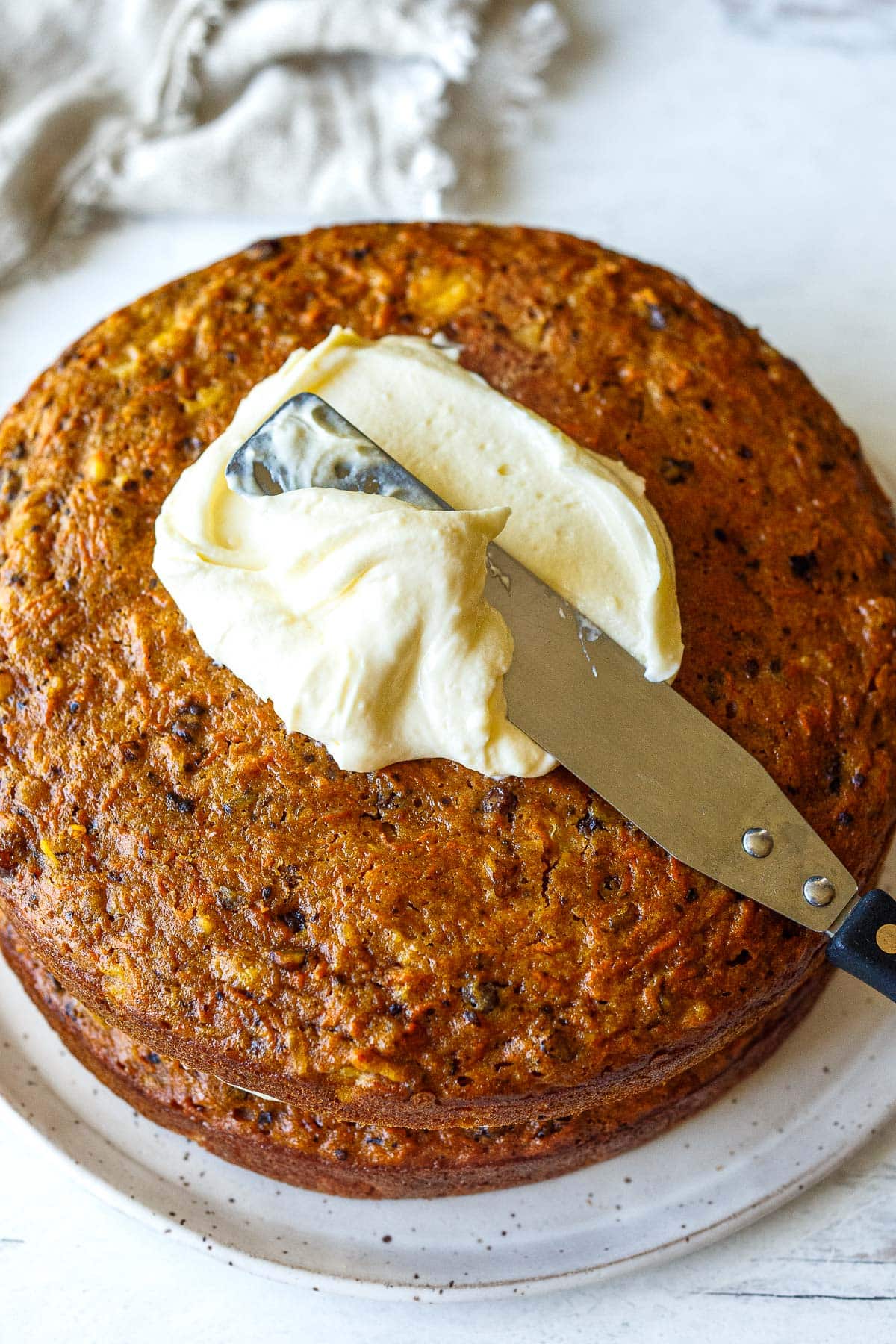 knife spreading cream cheese frosting onto baked carrot cake. 
