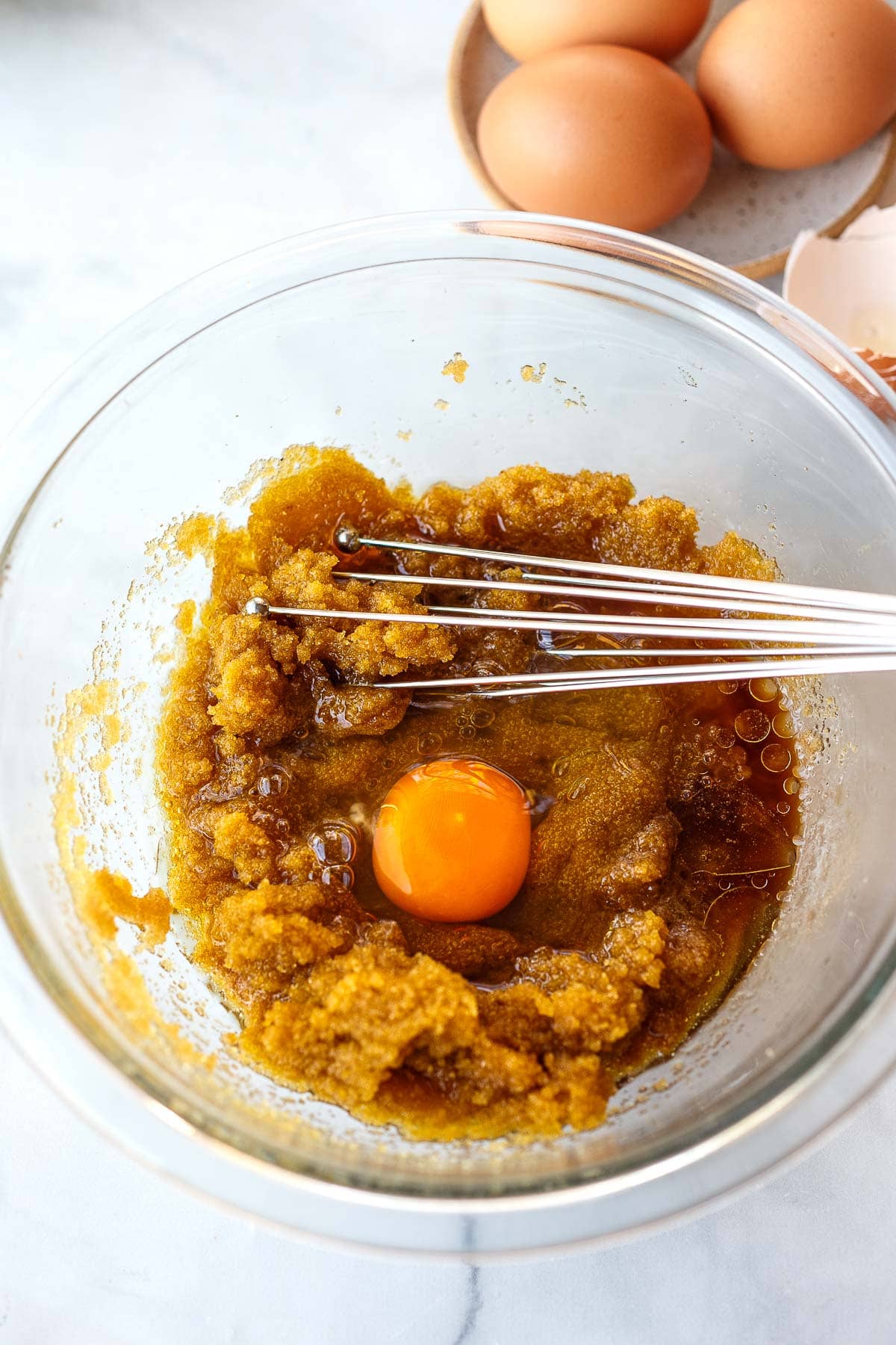 glass mixing bowl with brown sugar, oil, vanilla, and egg with a whisk. 
