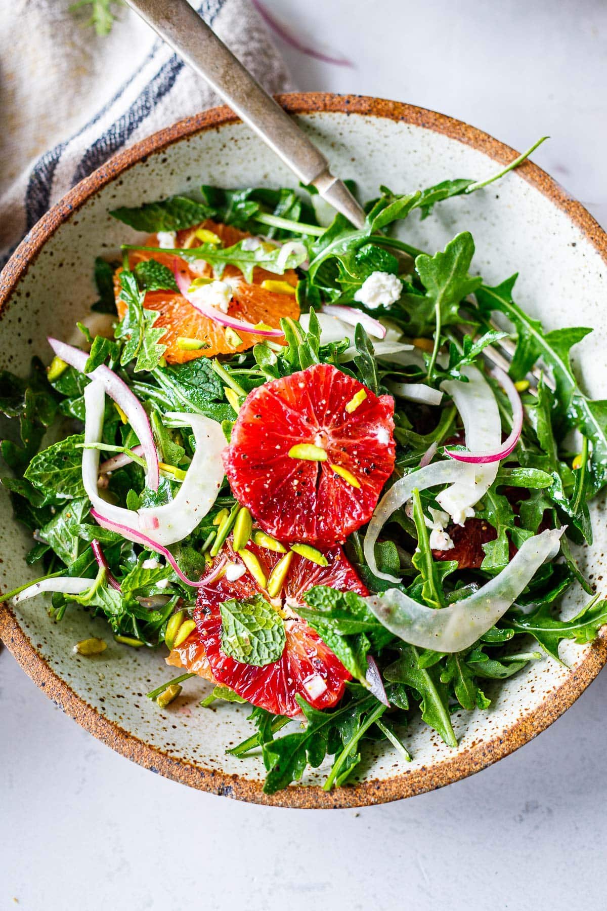 small bowl with fennel orange salad topped with crumbled goat cheese, sliced red onion, and pistachios. 