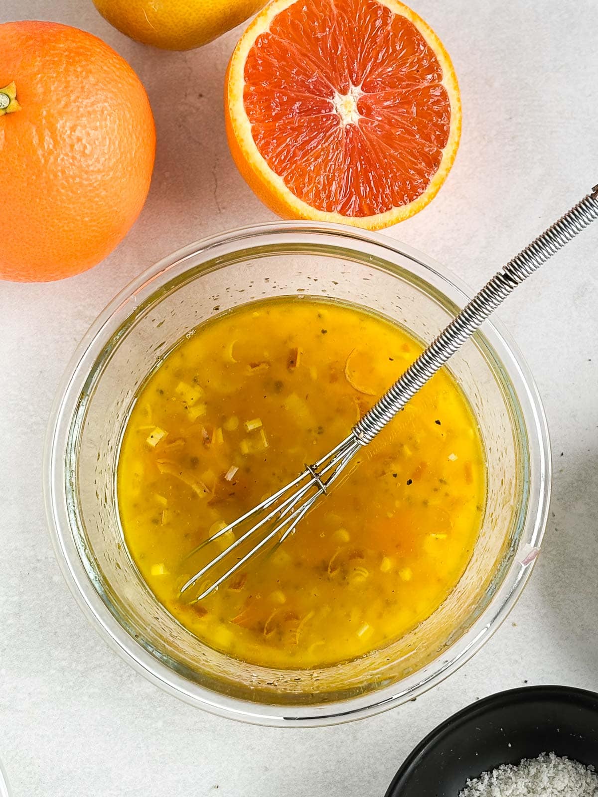 small bowl with whisk and citrus vinaigrette, surrounded by oranges. 