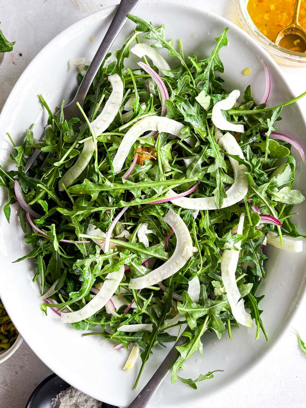 a platter of tossed arugula with fennel, red oion, mint and dressing. 