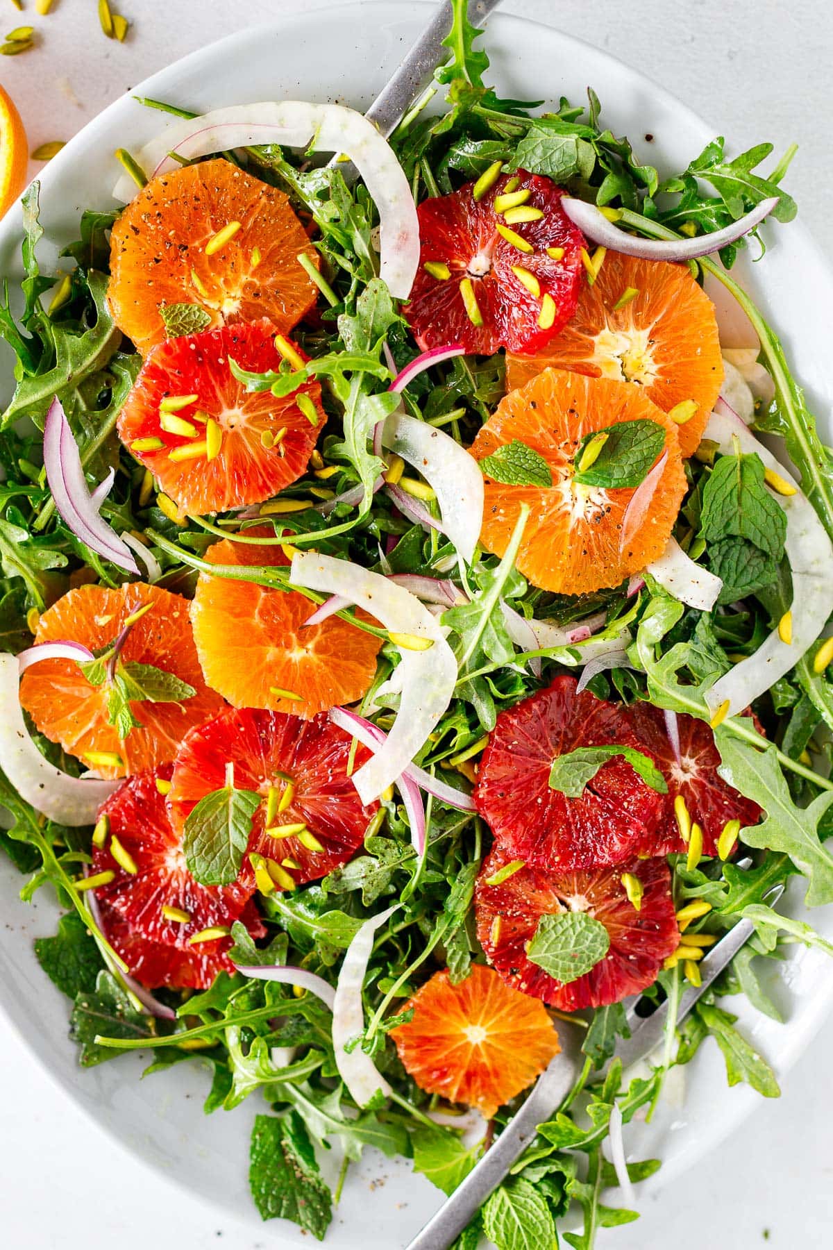 serving platter with fennel orange salad topped with sliced red onion and pistachios. 