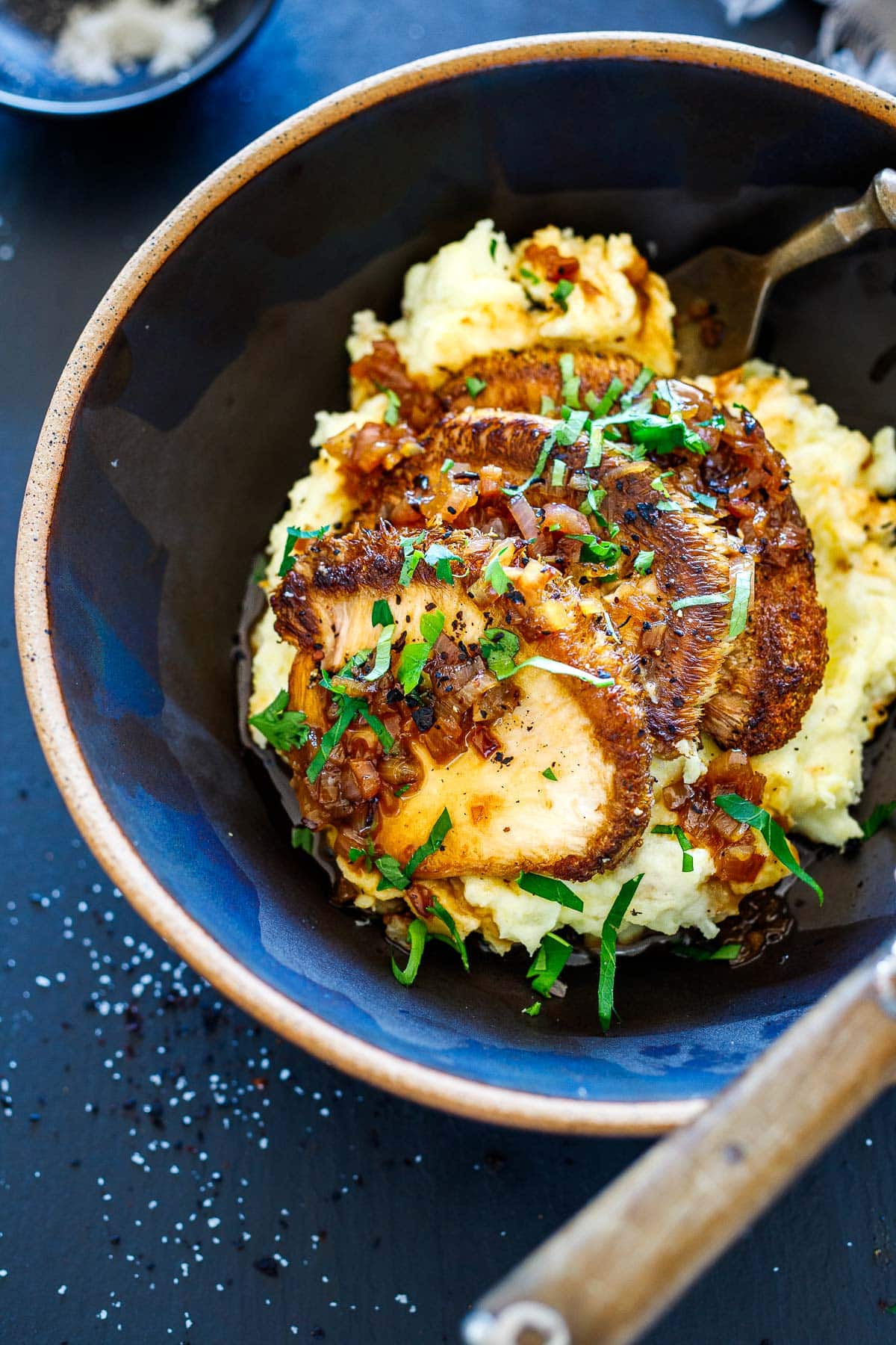sautéed lion's mane over mashed potatoes with pan sauce and fresh herbs drizzled over top in bowl with fork.