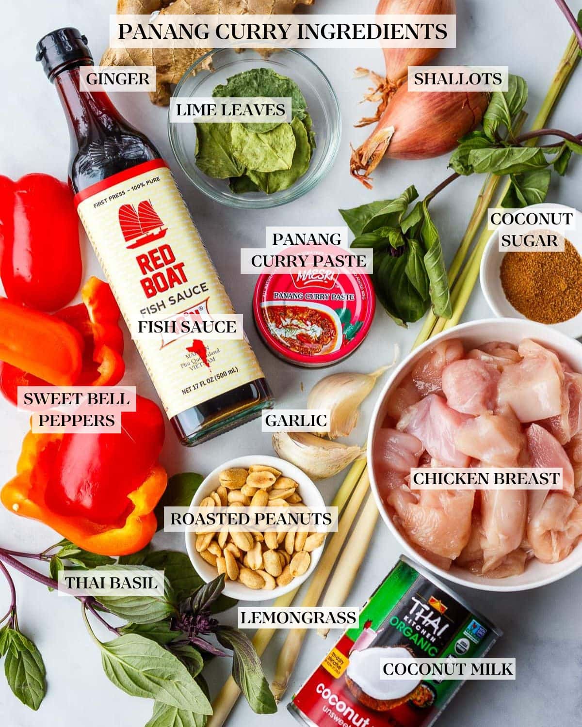 ingredients for panang curry- fresh ginger, kaffir lime leaves, shallot, fish sauce, bell peppers, panang curry paste, lemongrass, coconut sugar, garlic cloves, chicken cubes, peanuts, thai basil, and coconut milk can. 