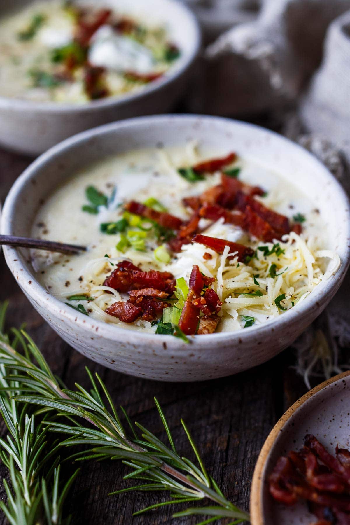 soup bowl with spoon with potato soup and crispy bacon, grated cheddar, green onions, and chives for garnish. 