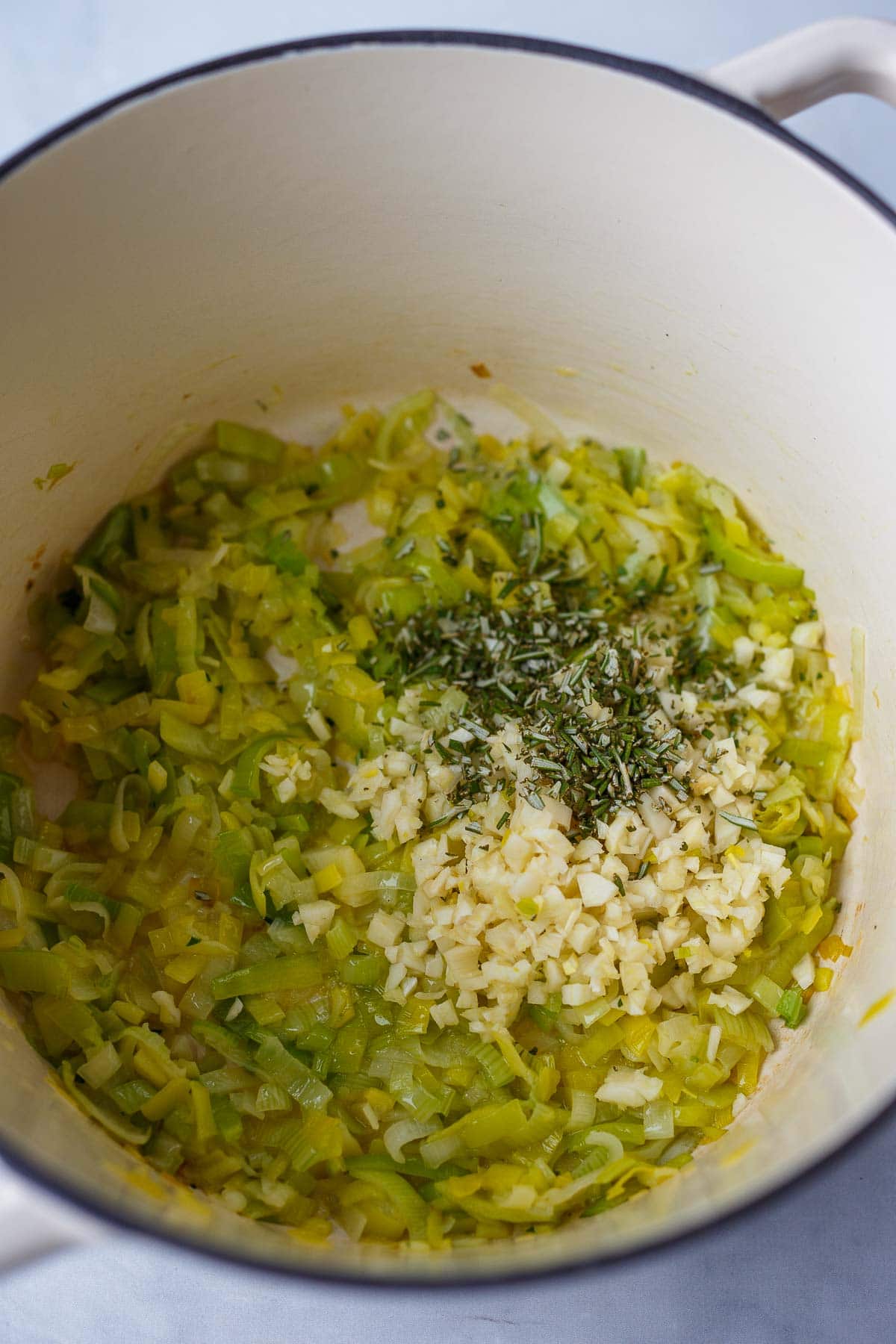 dutch oven with sautéed leeks and minced garlic and rosemary added on top.