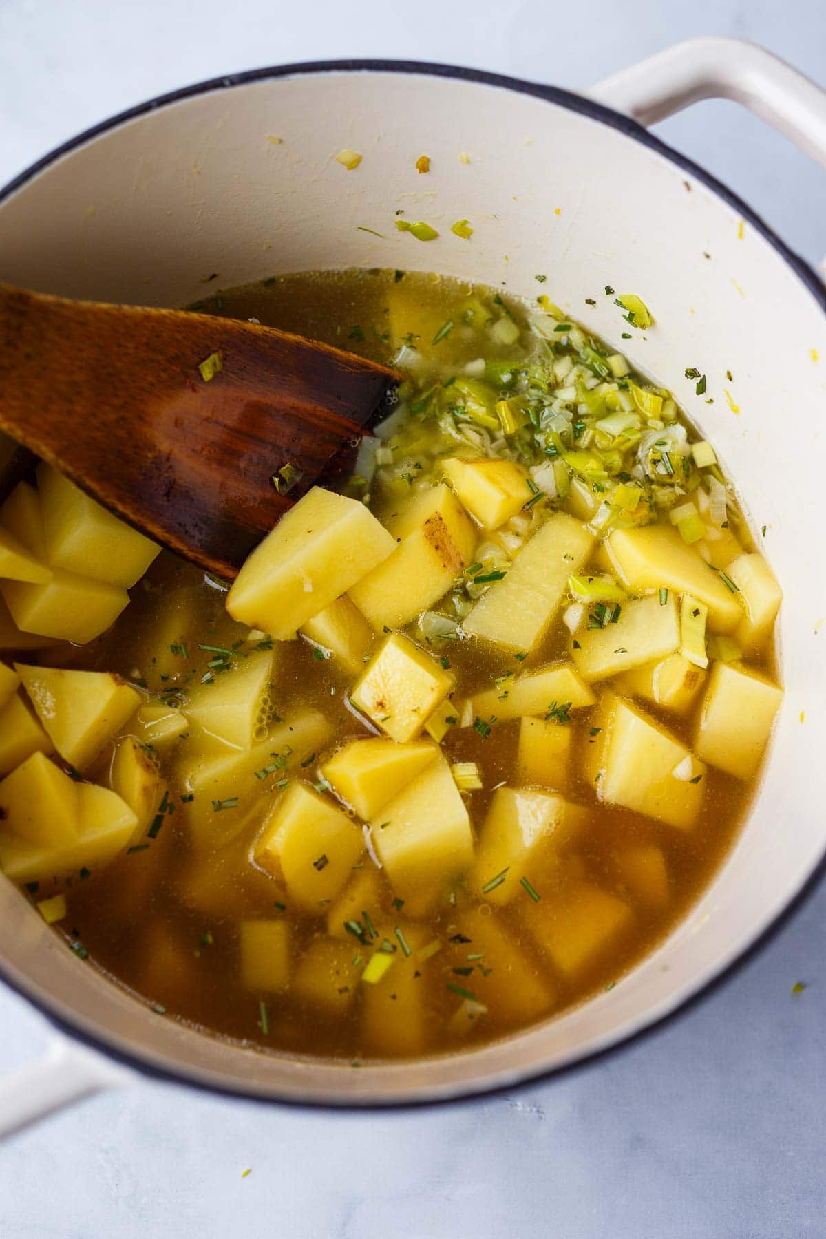 dutch oven with chopped potatoes in broth with sautéed leeks and wood spoon to stir. 
