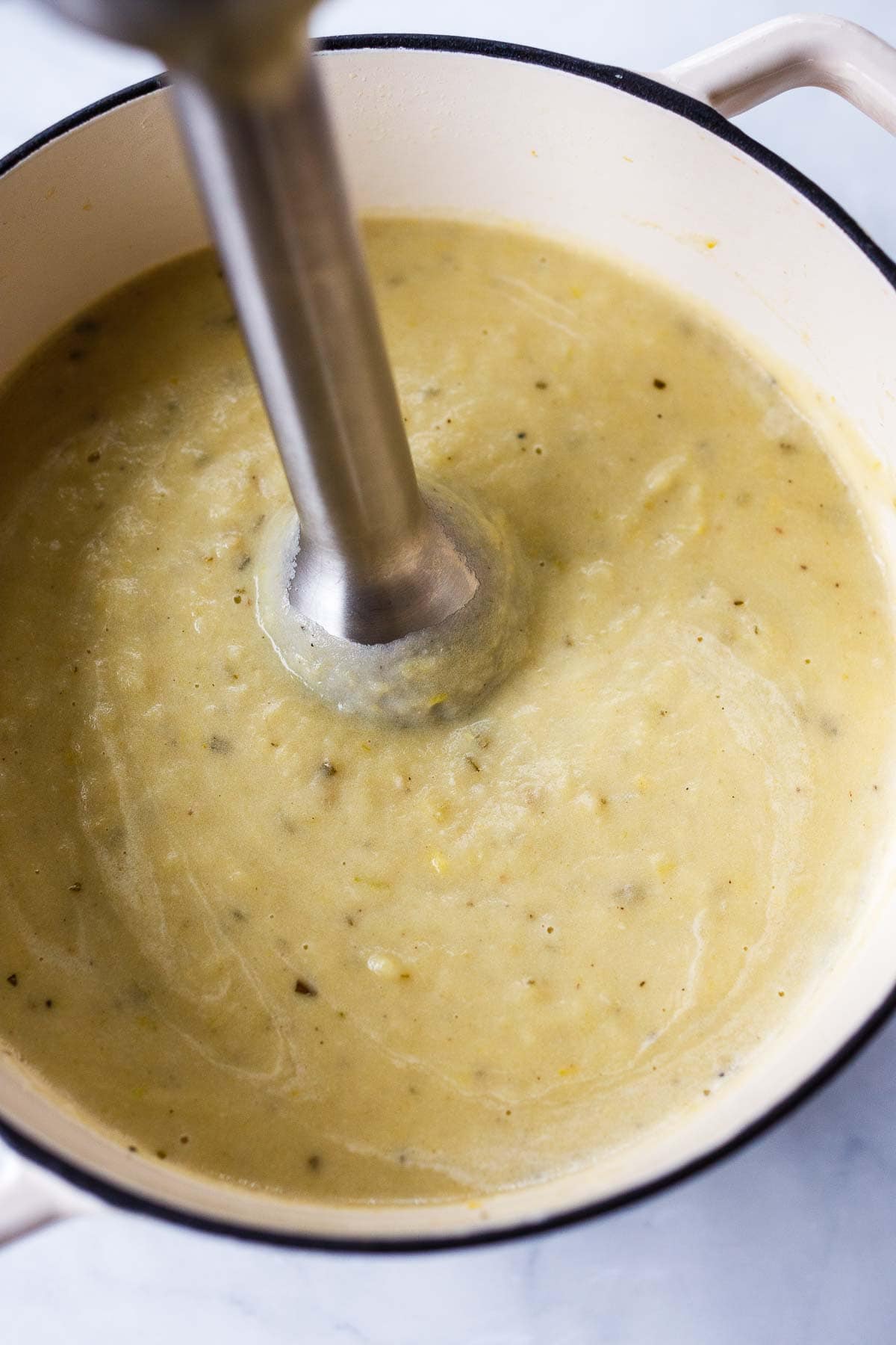 dutch oven with immersion blender in pot to create a creamy potato soup.