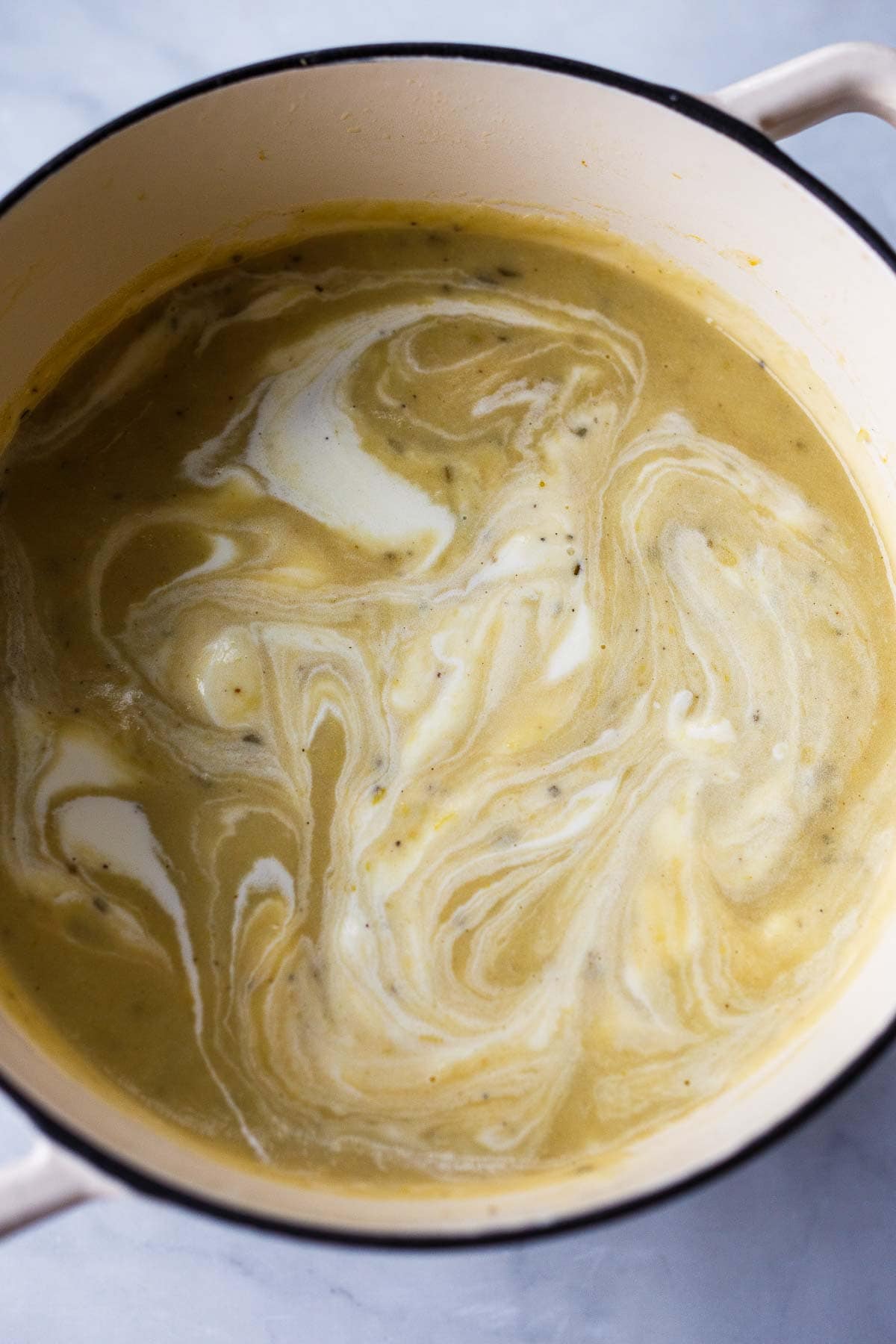 creamy potato soup in dutch oven with swirls of milk.