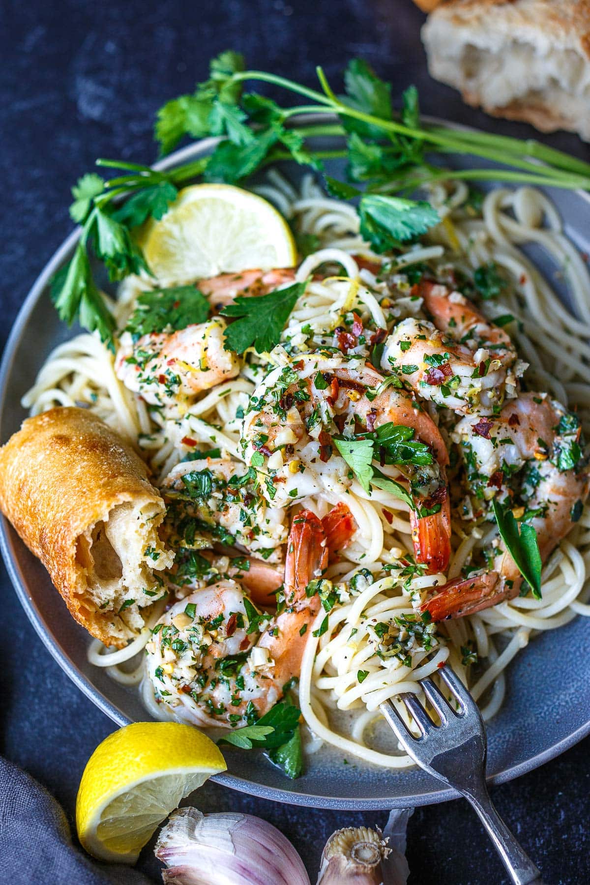 plate of shrimp scampi served over angel hair pasta with parsley garnish and served with crusty bread and lemon wedges.