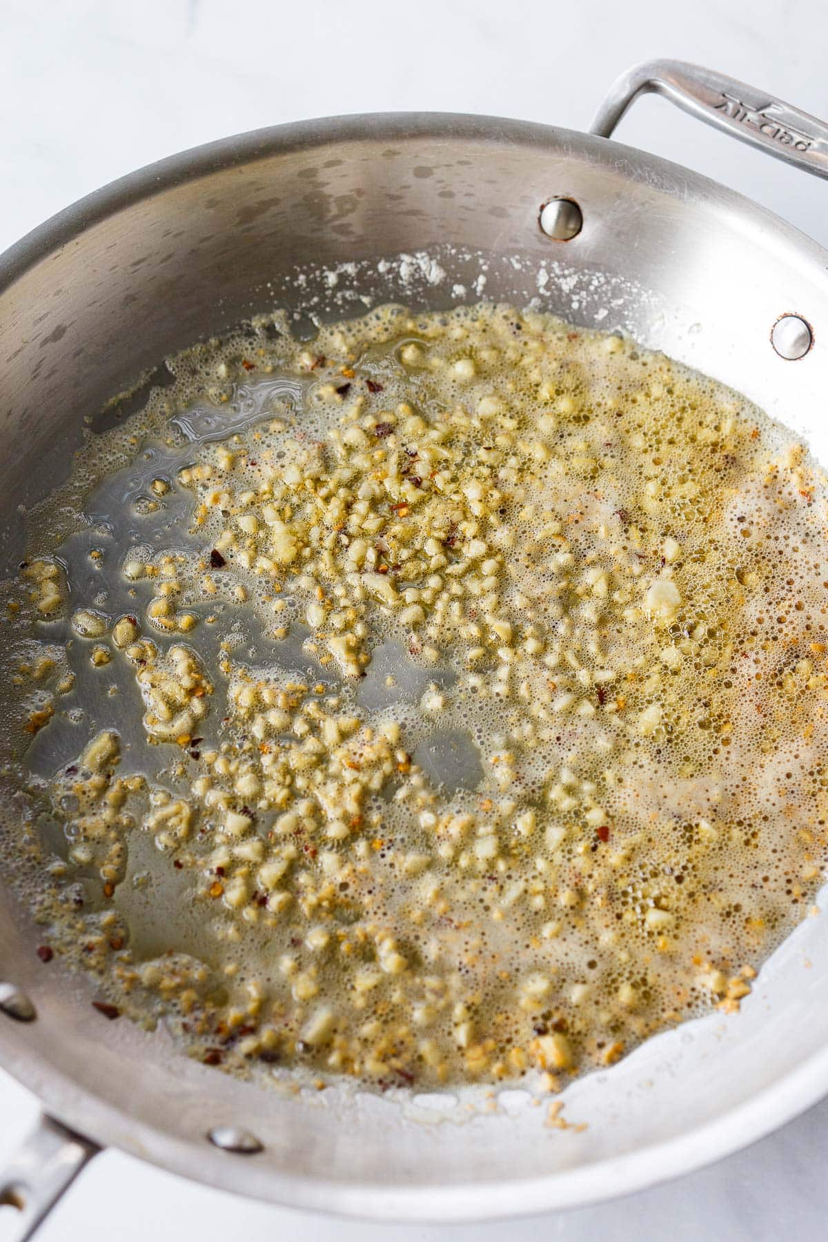 large stainless steel skillet with minced garlic sautéing in butter and oil.