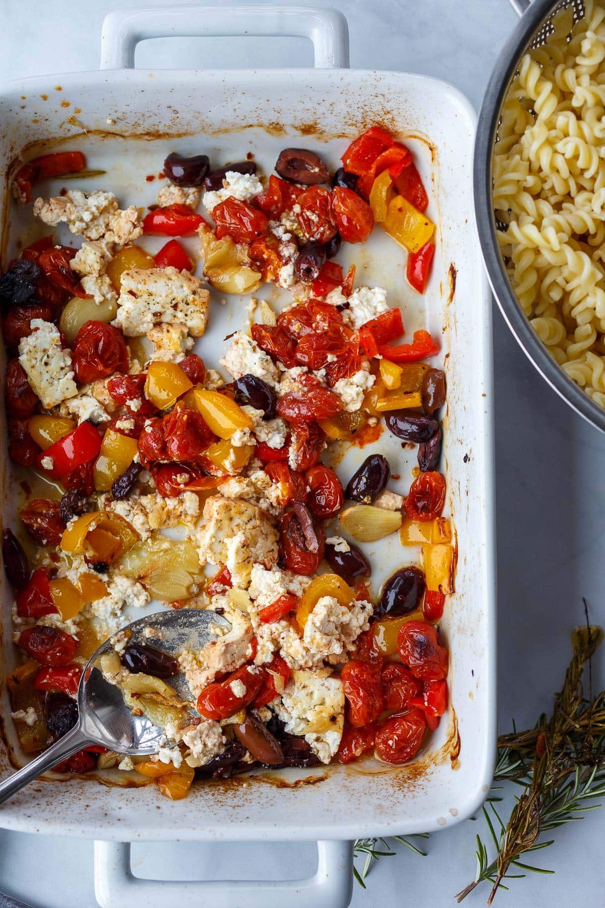 spoon mashing baked feta and garlic cloves in the dish of veggies. 