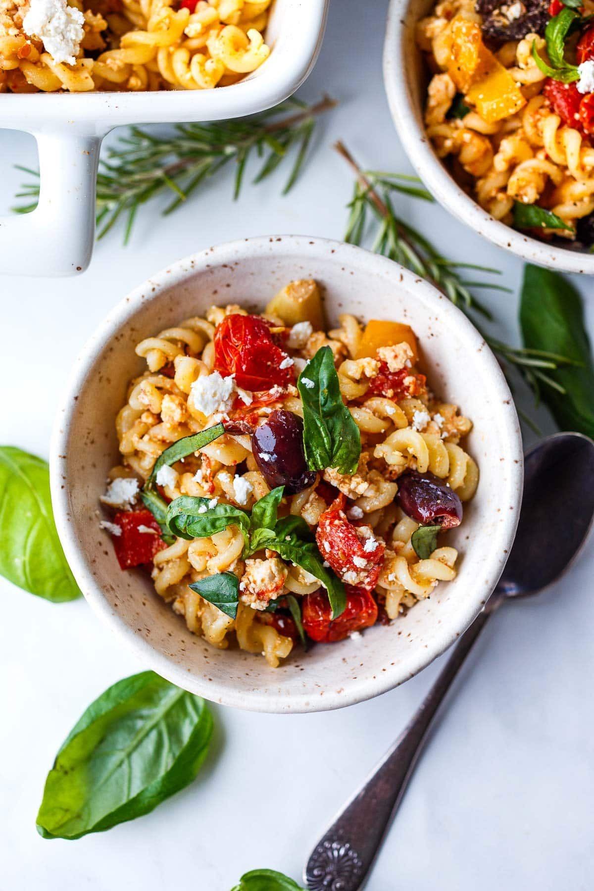 bowl of baked feta pasta with olives, roasted tomatoes, and fresh basil. 