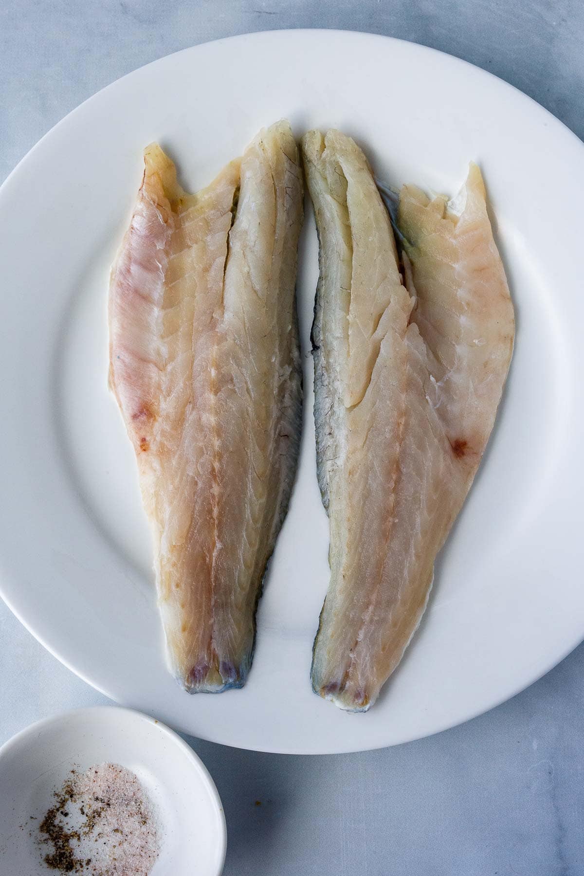 two branzino fillets flesh side up on a plate.