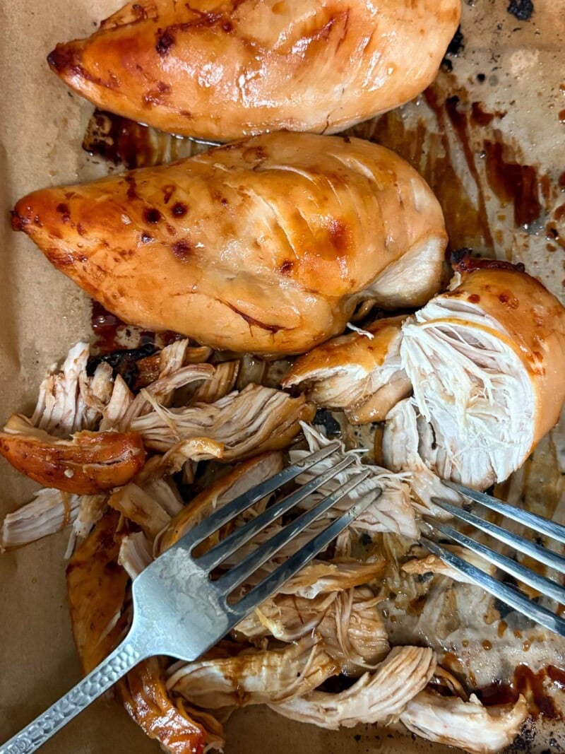 two forks pulling apart baked sesame chicken breasts to make shredded chicken.