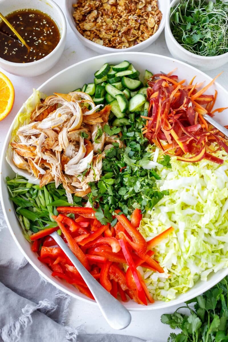 large salad bowl with serving utensils showing the chinese chicken salad before mixing, with each ingredient in neat sections.