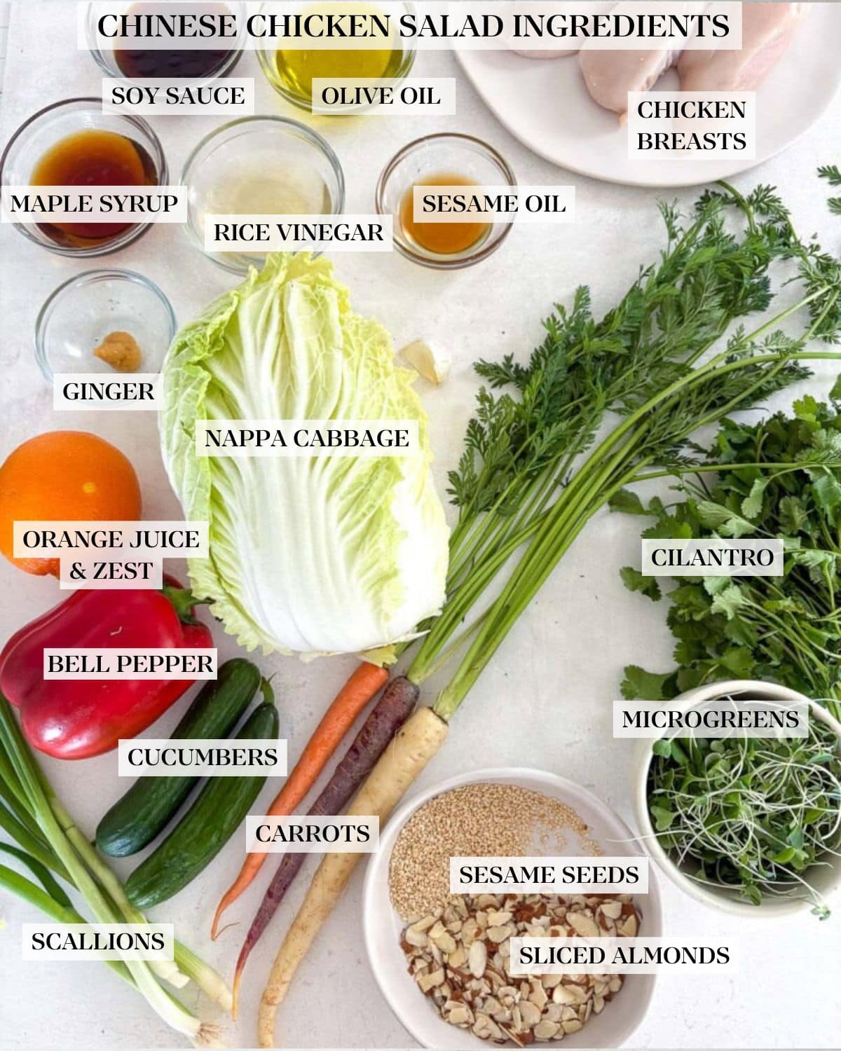 chinese chicken salad ingredients laid out on the counter - plate of chicken breasts, small bowls of sauces, napa cabbage, carrots, cucumber, green onions, almonds and sesame seeds, microgreens, and cilantro.