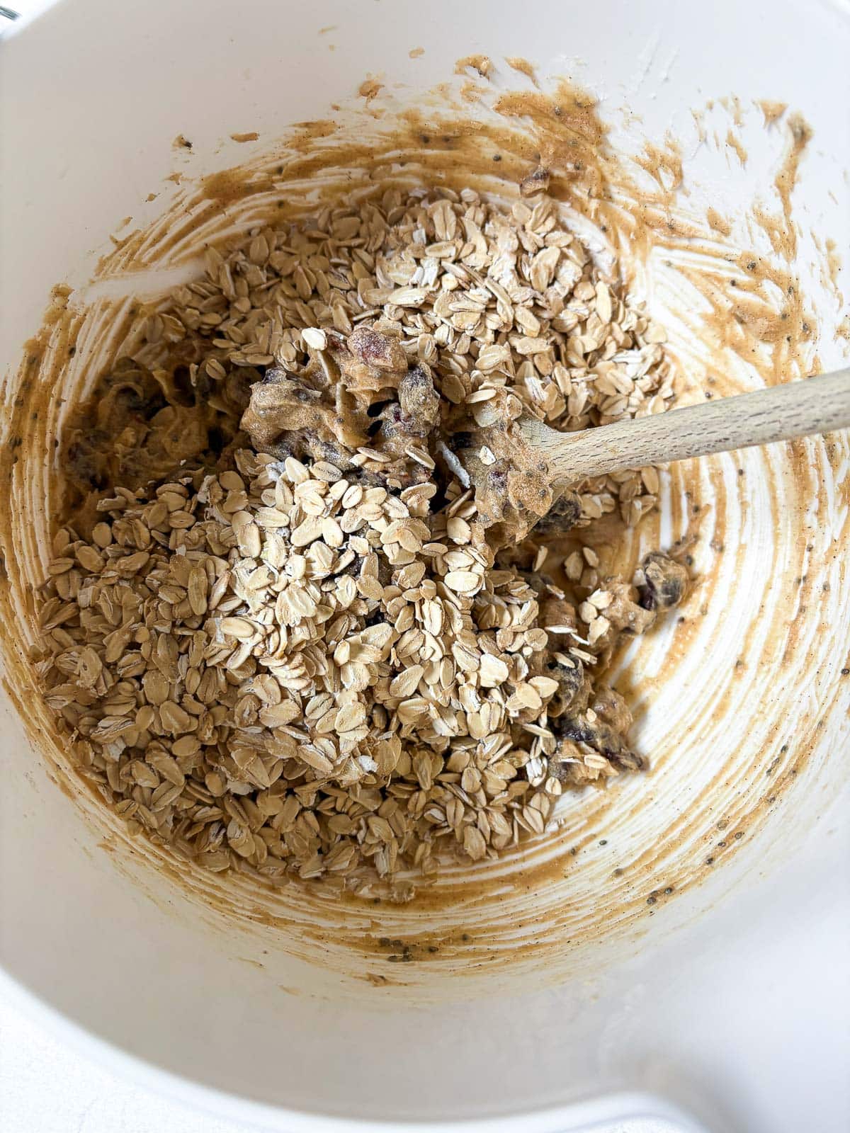 mixing bowl with cowgirl cookies batter and a wood spoon folding in the rolled oats. 