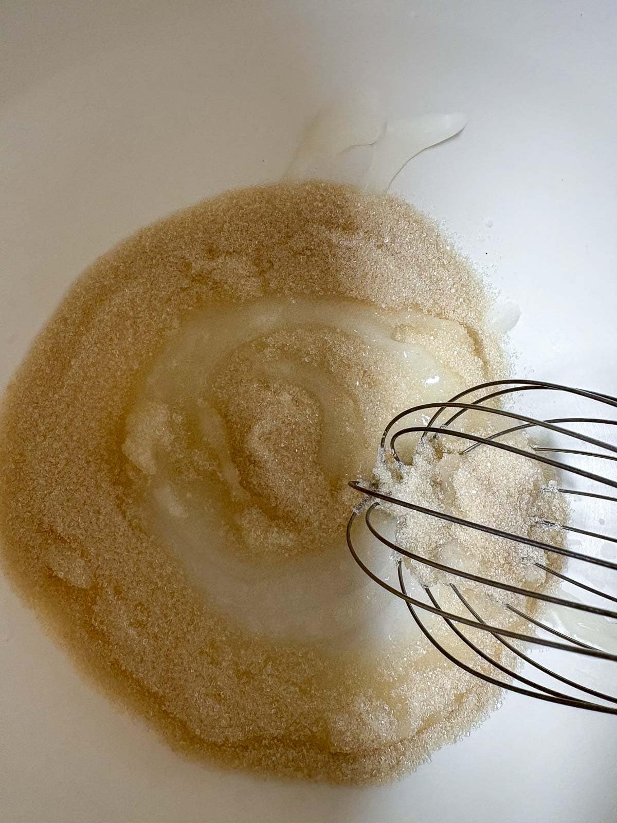mixing bowl with melted coconut oil and sugar with a whisk beginning to mix.