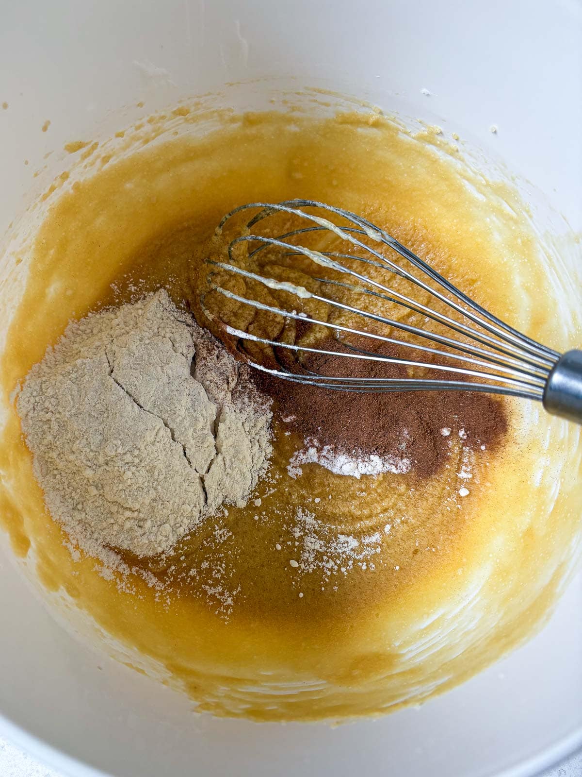 mixing bowl of cowgirl cookies batter with flour and spices added to the bowl with a whisk.