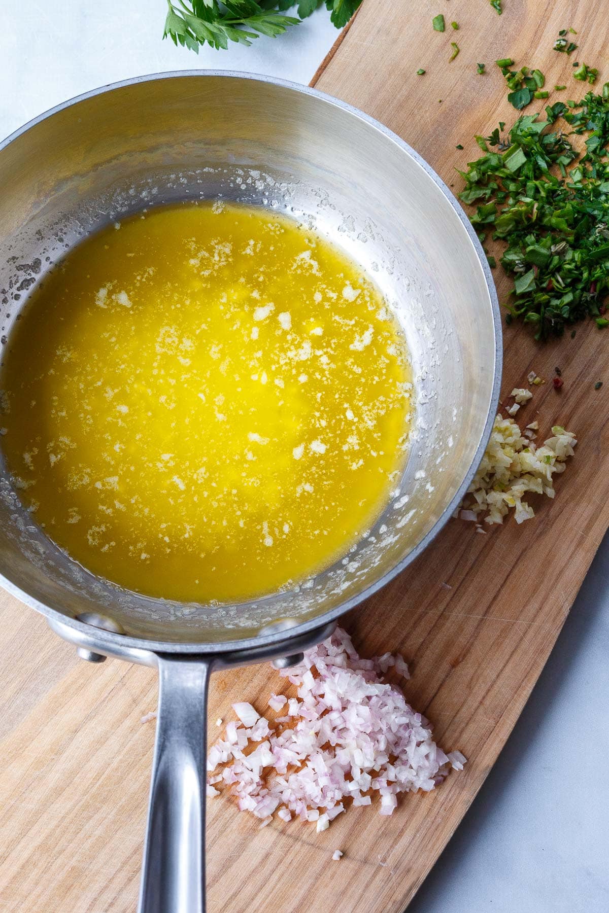 saucepan with lemon butter sauce on wood board with minced shallot, garlic, and fresh herbs.