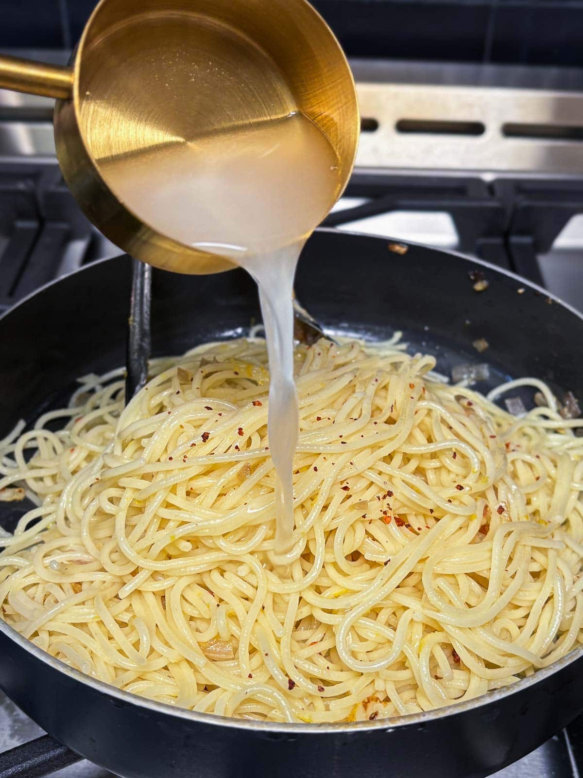 pouring hot pasta water into the large skillet with pasta.
