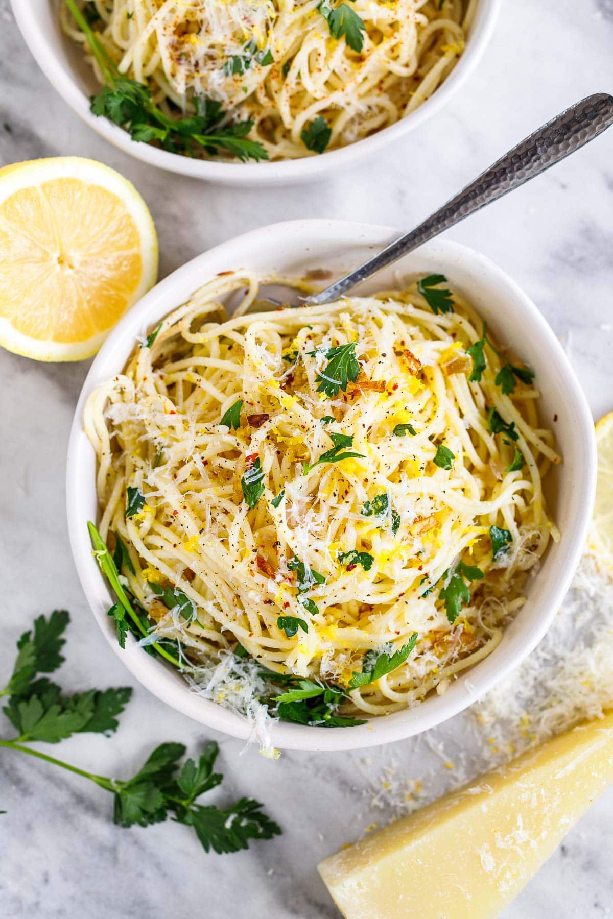 bowl of lemon pasta with pecorino, lemon zest, and parsley, beside lemon half, fresh parsley, and pecorino wedge.