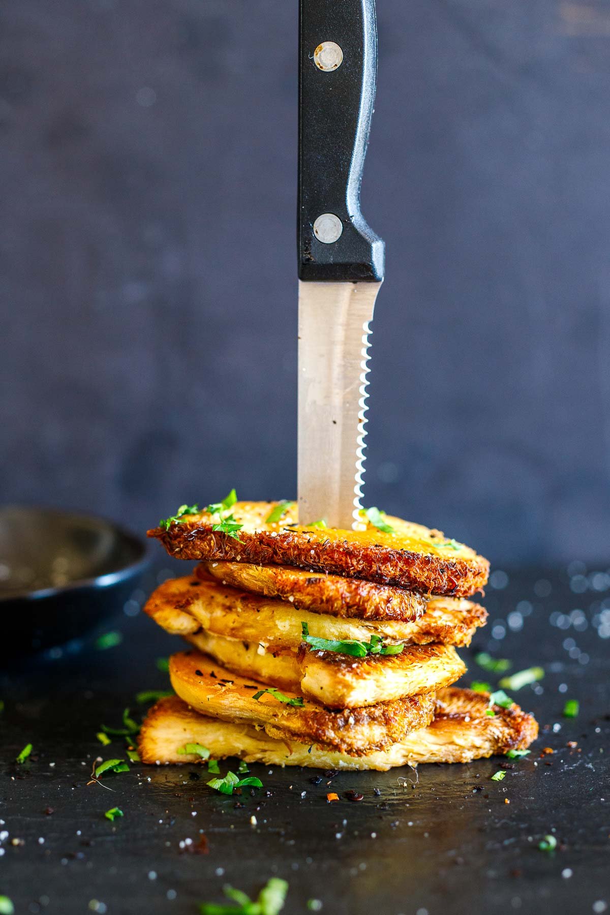 steak knife pointing down, sticking into a stack of seared lion's mane mushrooms with fresh herbs.