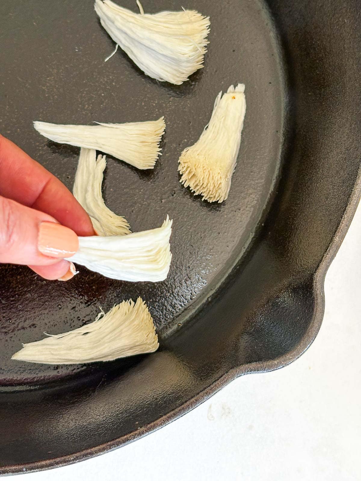 hand placing shredded lion's mane in cast iron skillet.