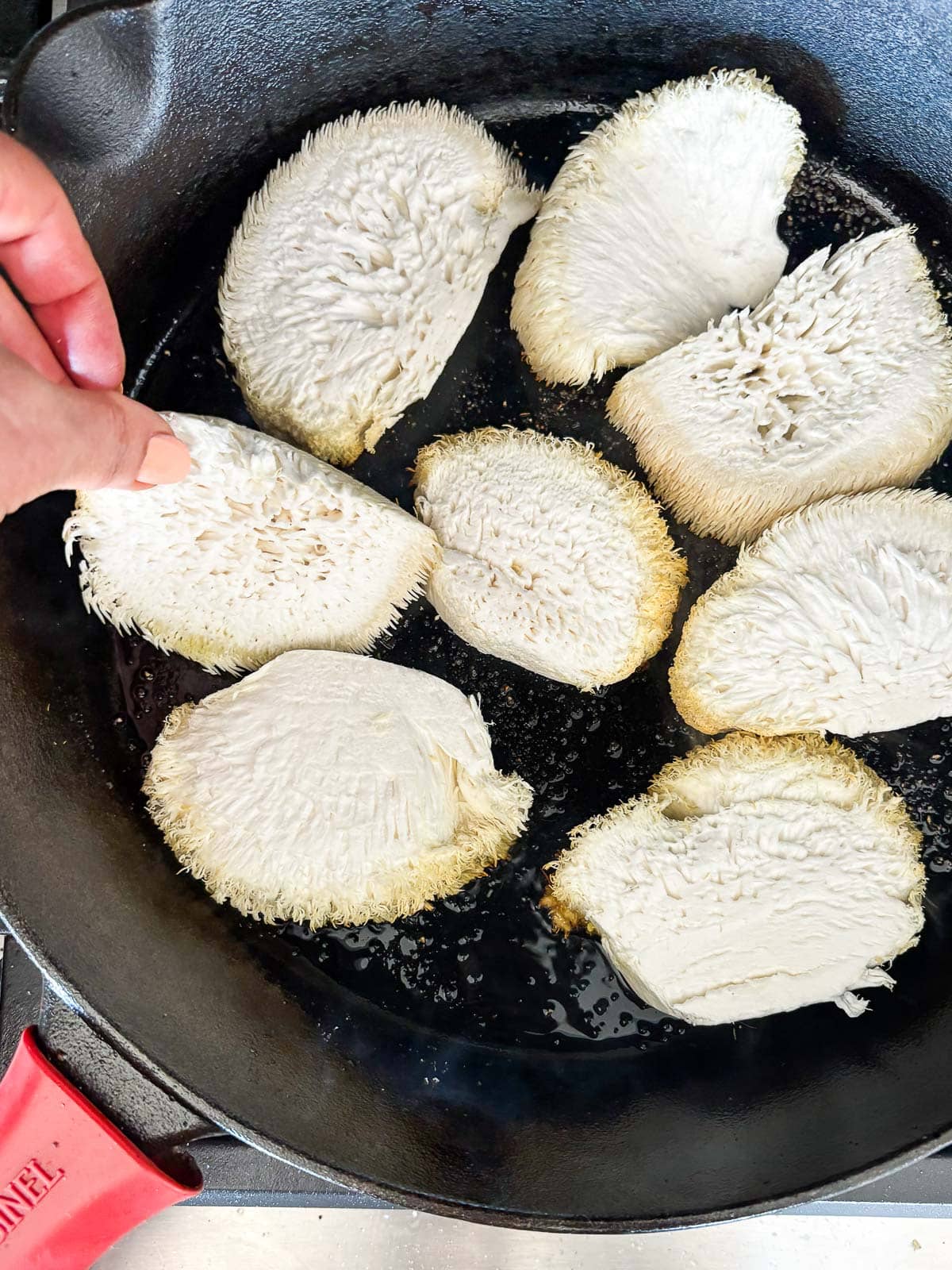 hand arranging sliced lion's mane mushroom in cast iron skillet with oil.