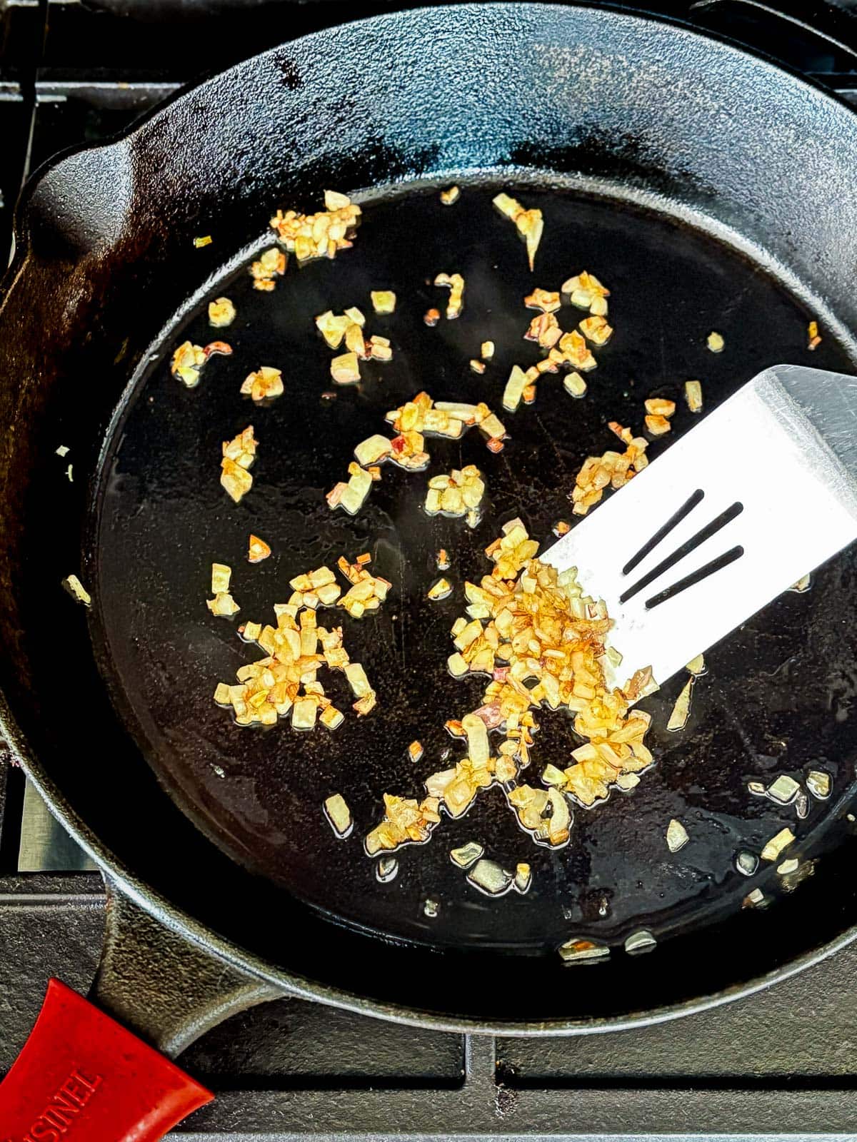 metal spatula stirring sautéed shallot in cast iron skillet. 