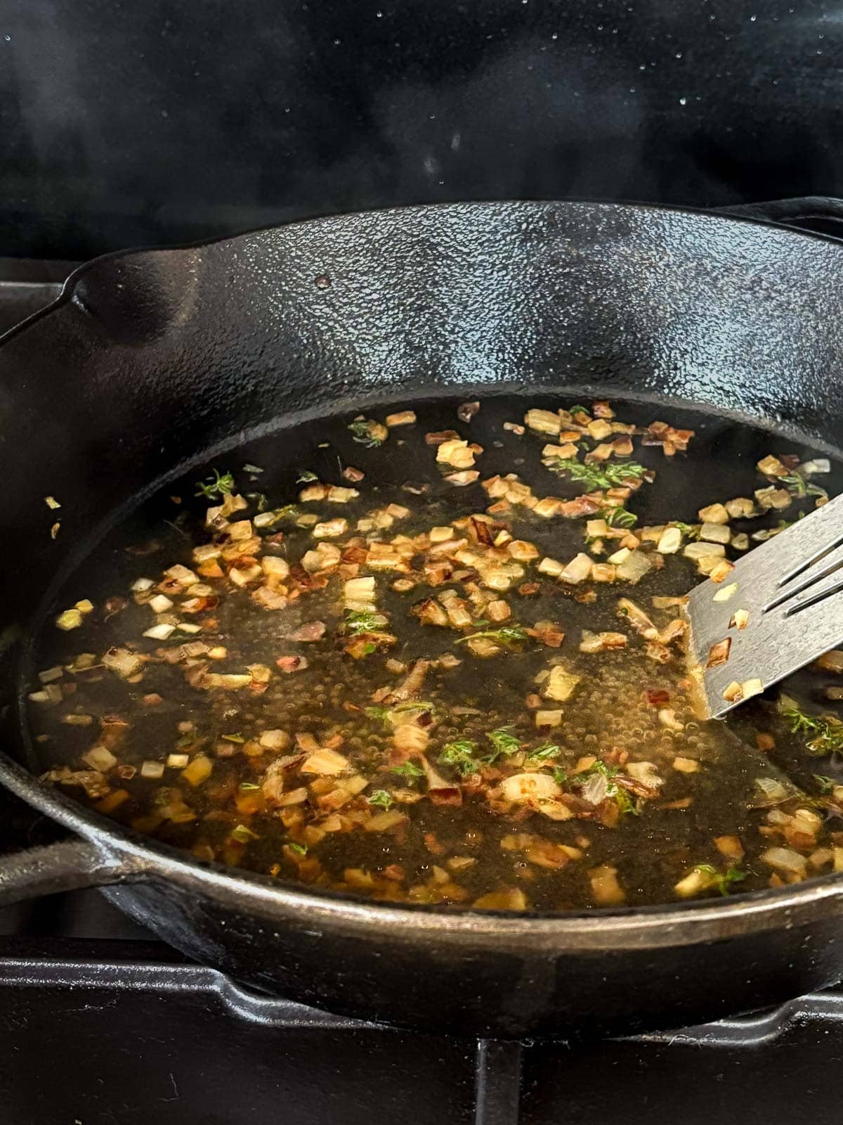 metal spatula stirring browned bits of shallot and wine in cast iron skillet to make pan sauce.