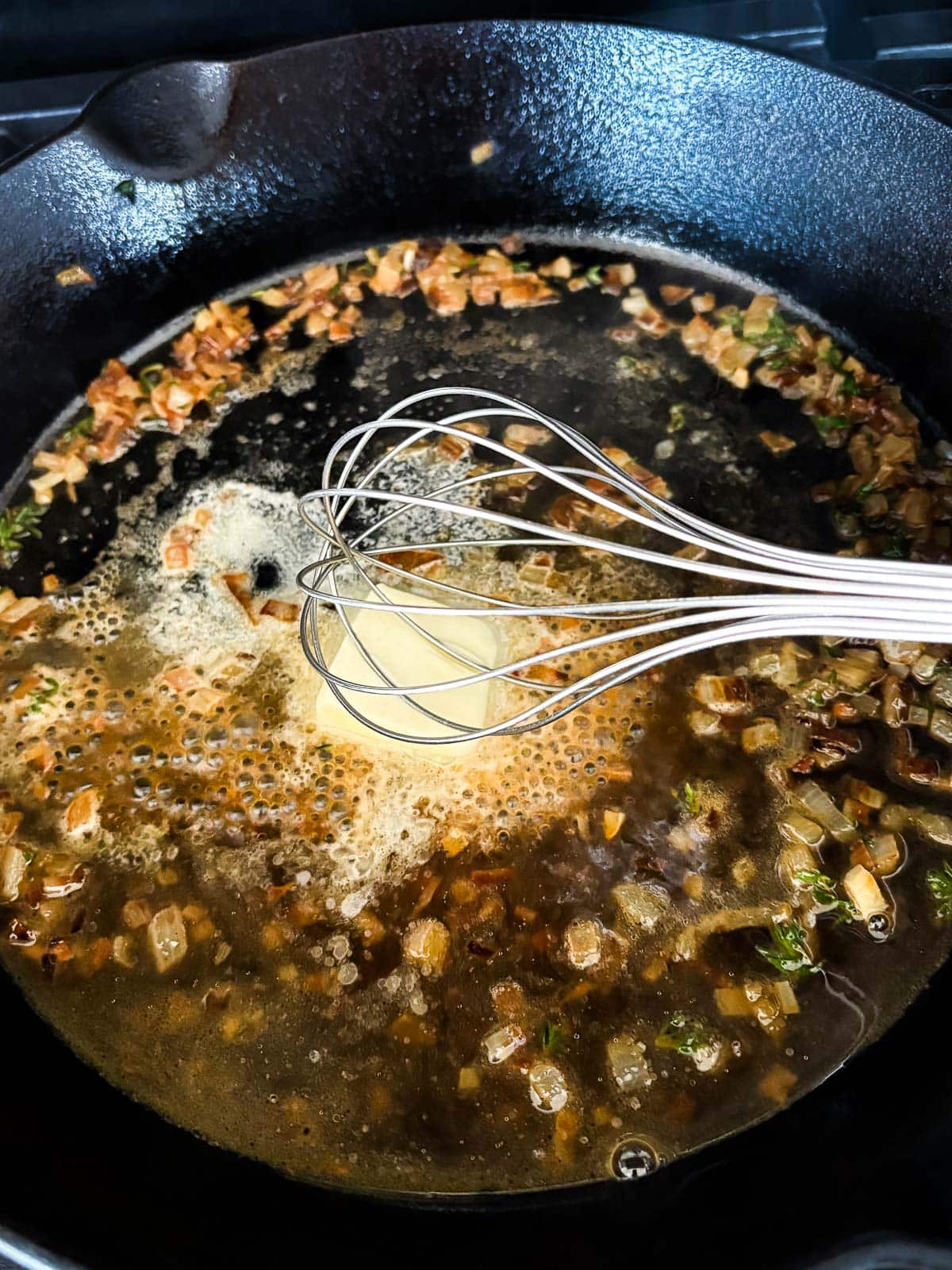 metal whisk stirring in butter into pan sauce in cast iron skillet. 