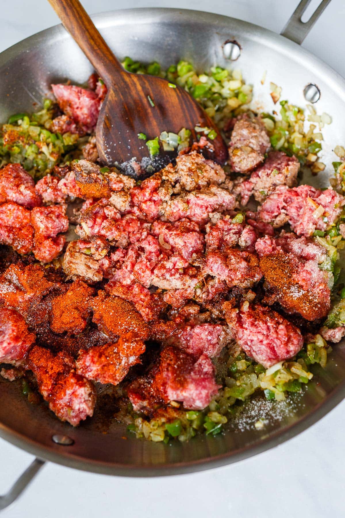 skillet with ground beef added to sautéed veggies and spices added on top. 