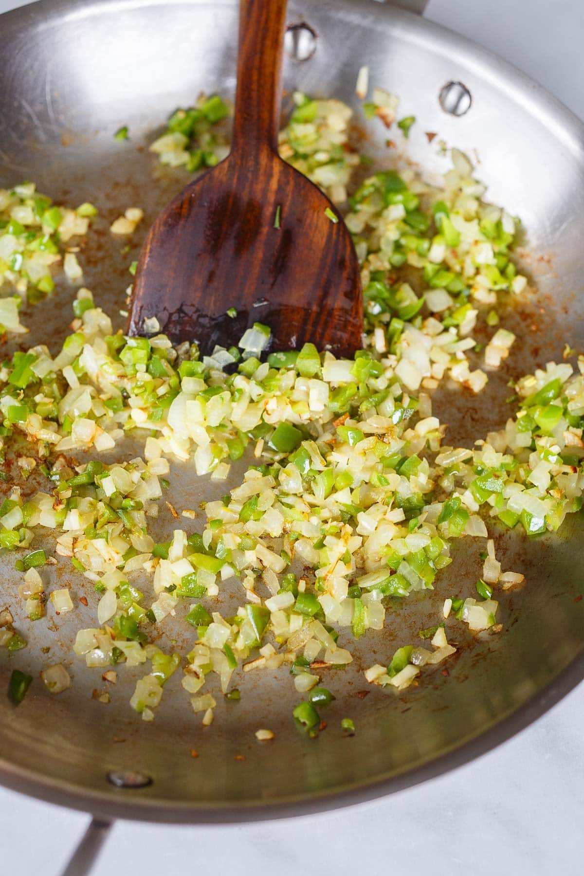 skillet with minced onion and pepper sautéing with wooden spatula. 