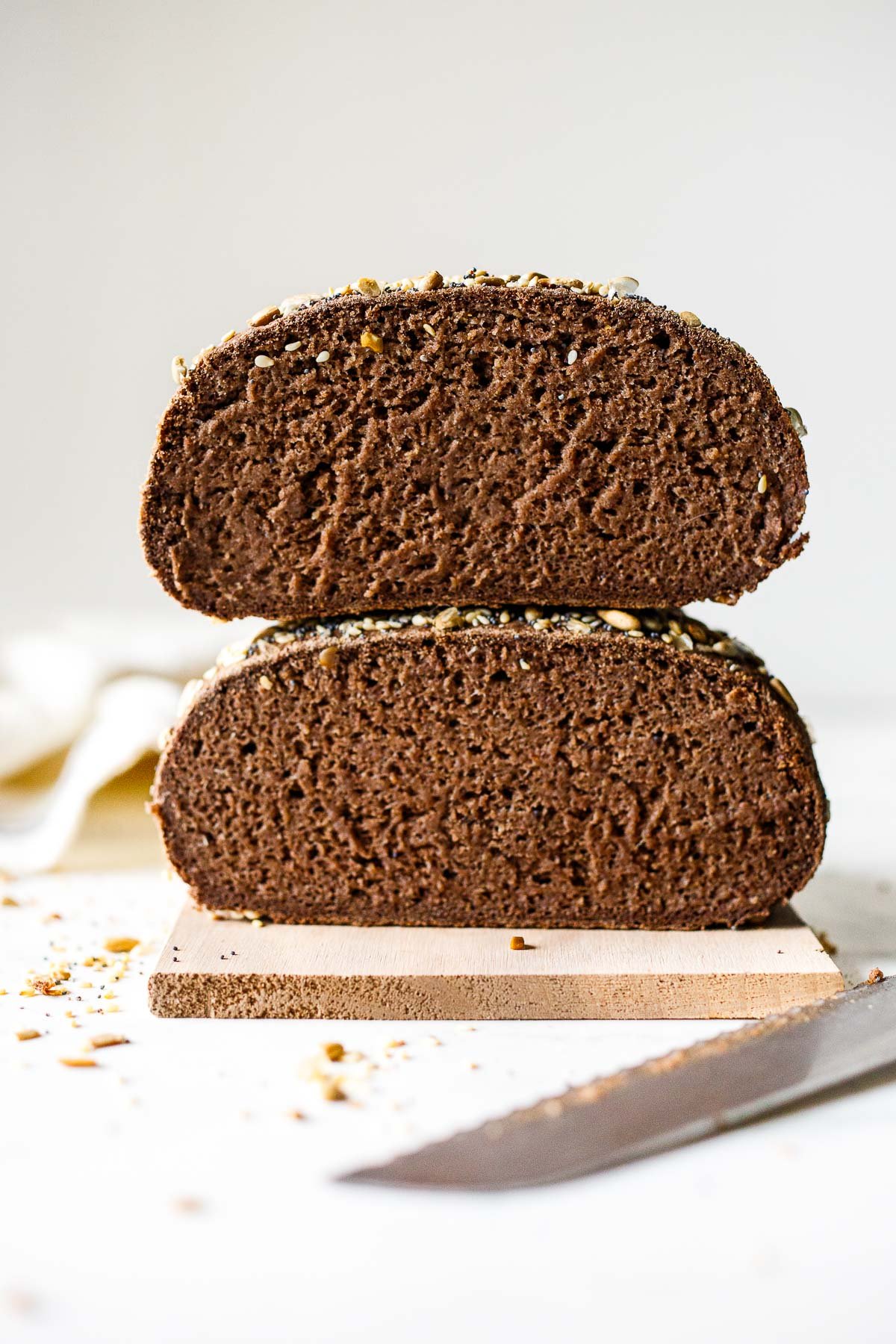 two halves of gluten free bread stacked on top of each other to show interior texture, on a wood board with a serrated knife in front.
